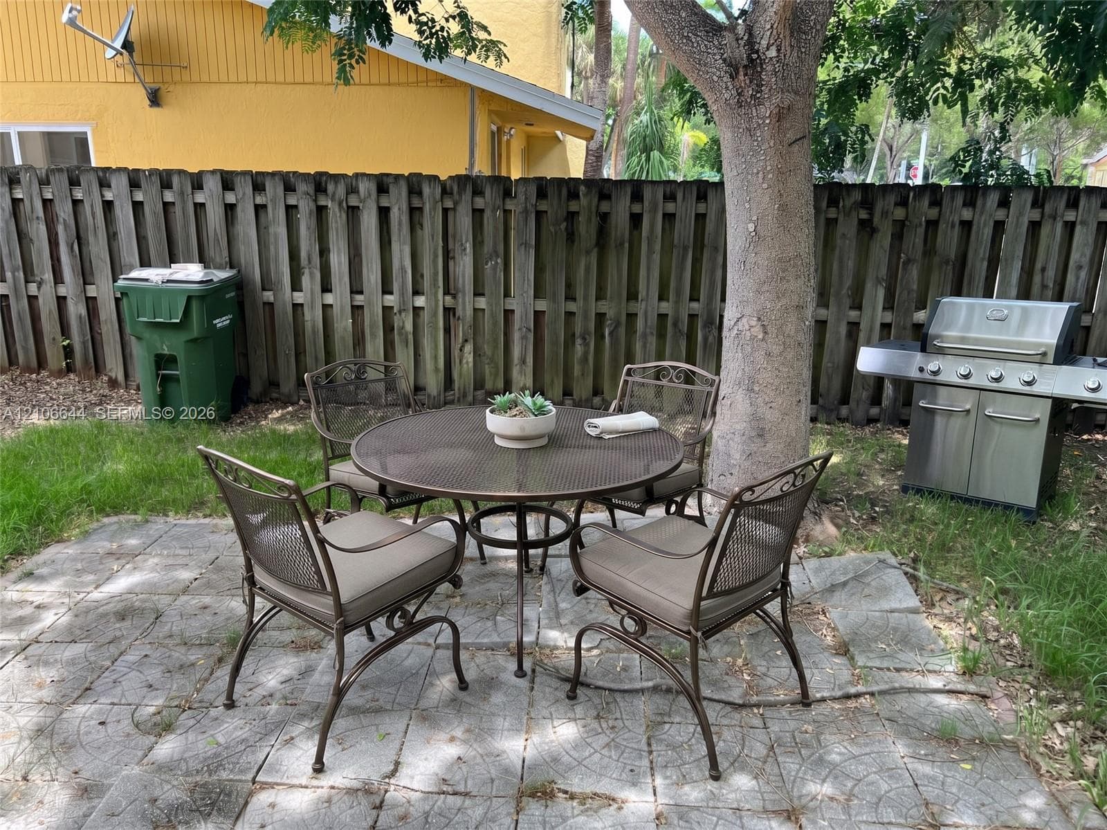 Rear yard featuring a paved patio area, wood-plank privacy fencing, and a mature tree