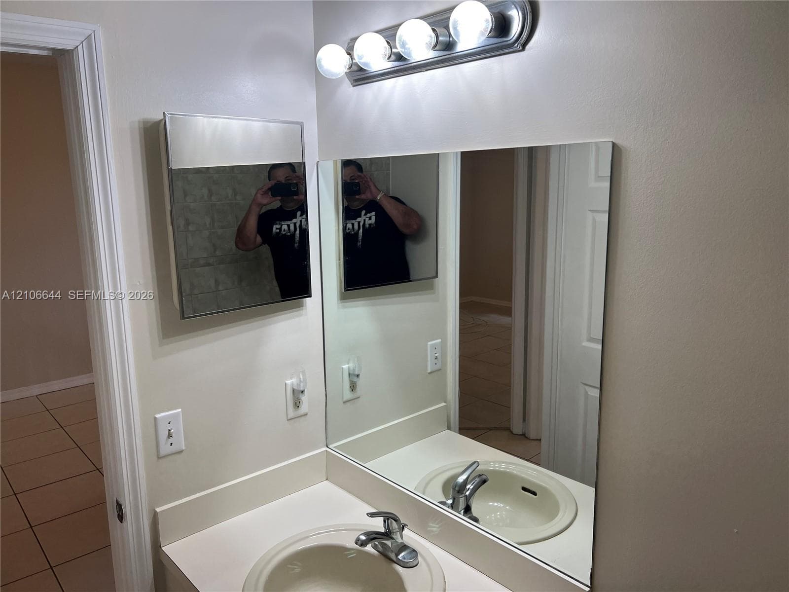 Wall-mounted medicine cabinet with a mirrored door, large rectangular wall mirror, vanity countertop with an integrated sink, polished chrome faucet, and multi-bulb vanity light fixture