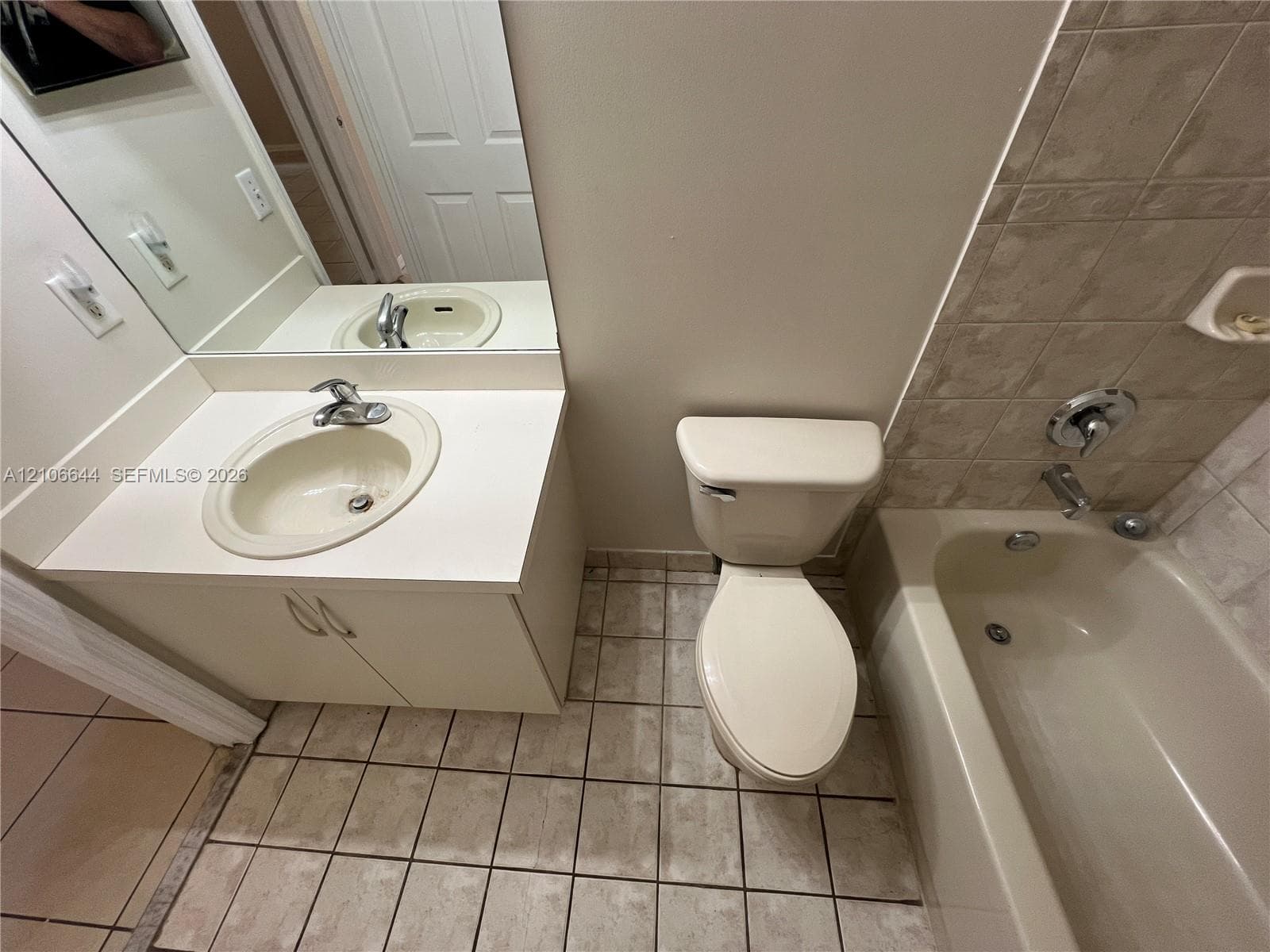 Bathroom featuring tile flooring, a vanity with a solid-surface countertop and integrated sink, a commode, and a tub-shower combination with tile surround