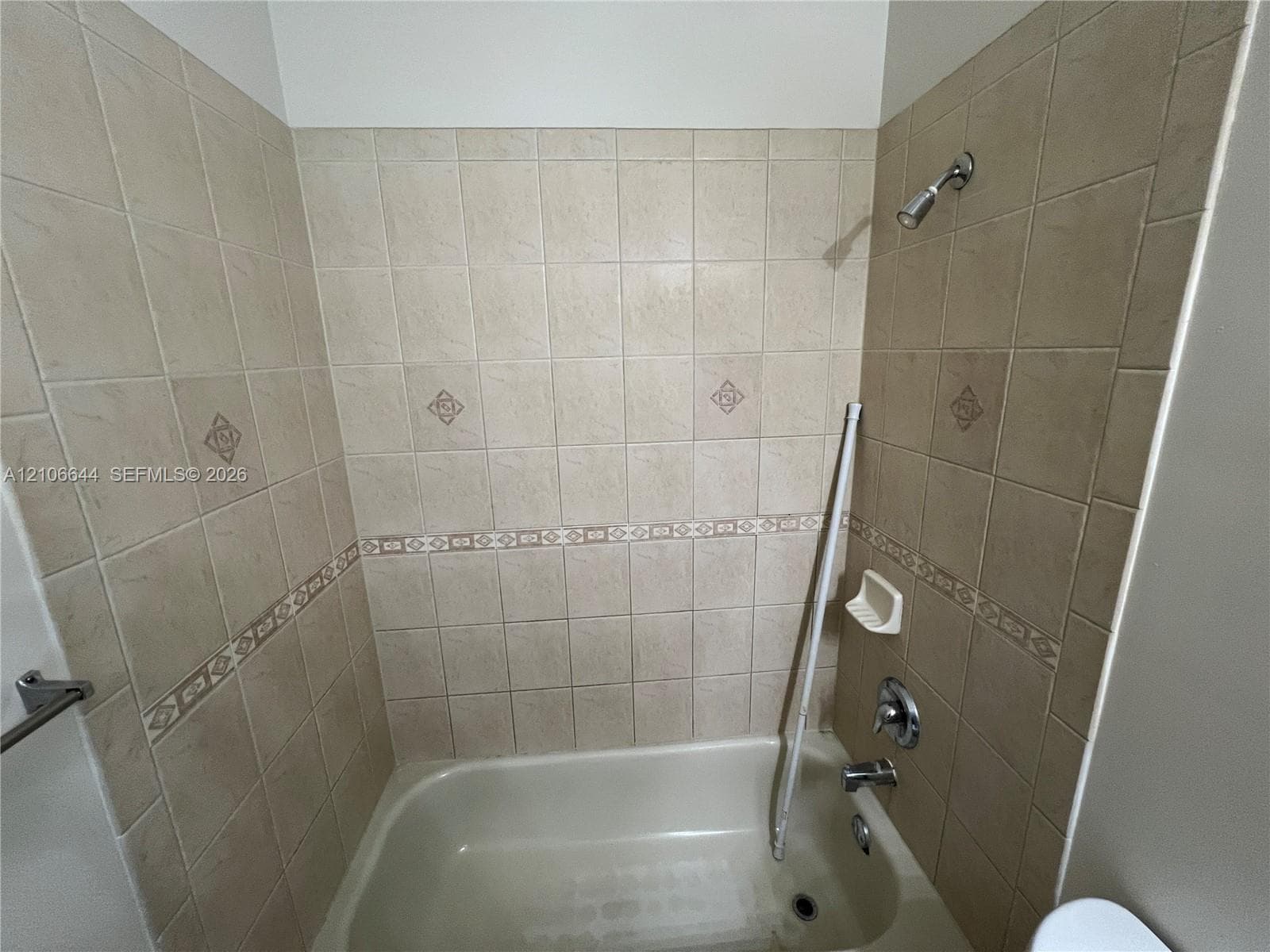 Bathtub with an integrated shower, beige ceramic tile surround, decorative tile inlay, and built-in soap dish