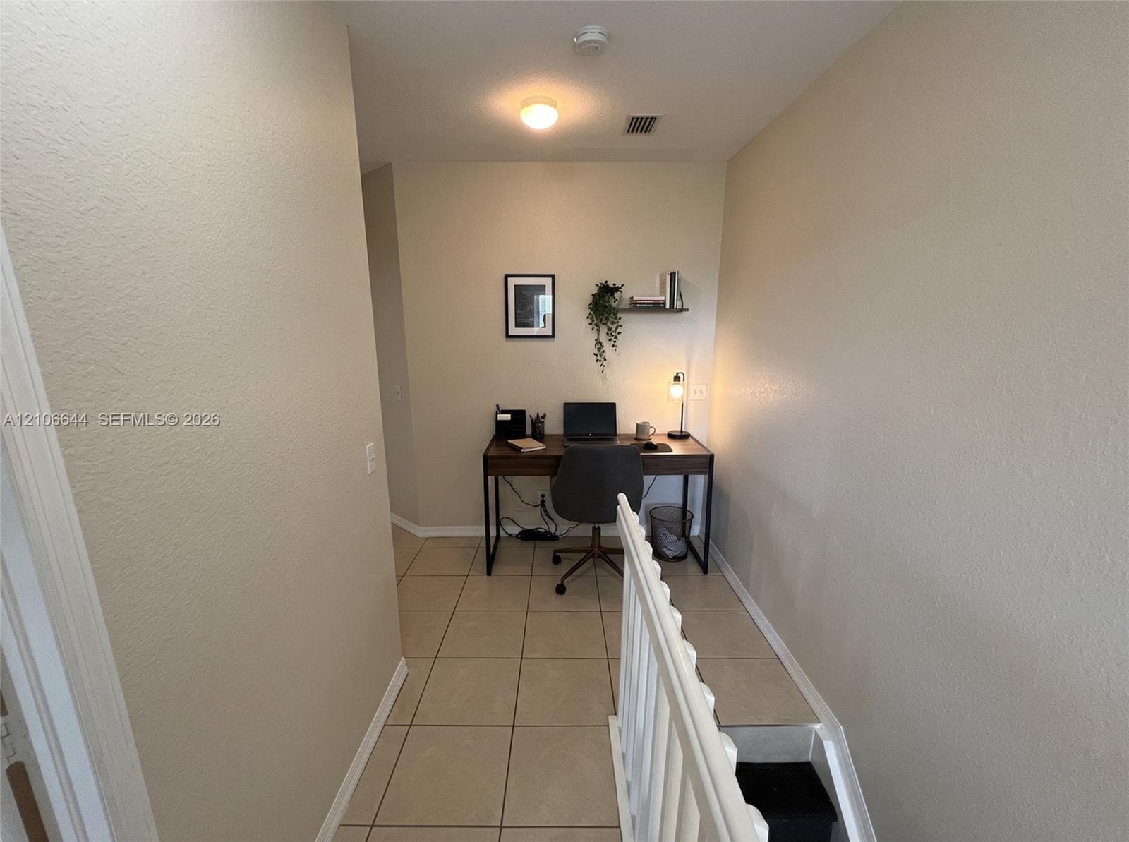Neutral-toned interior space featuring light-colored square tile flooring, a wall-mounted floating shelf, and white balustrade railings