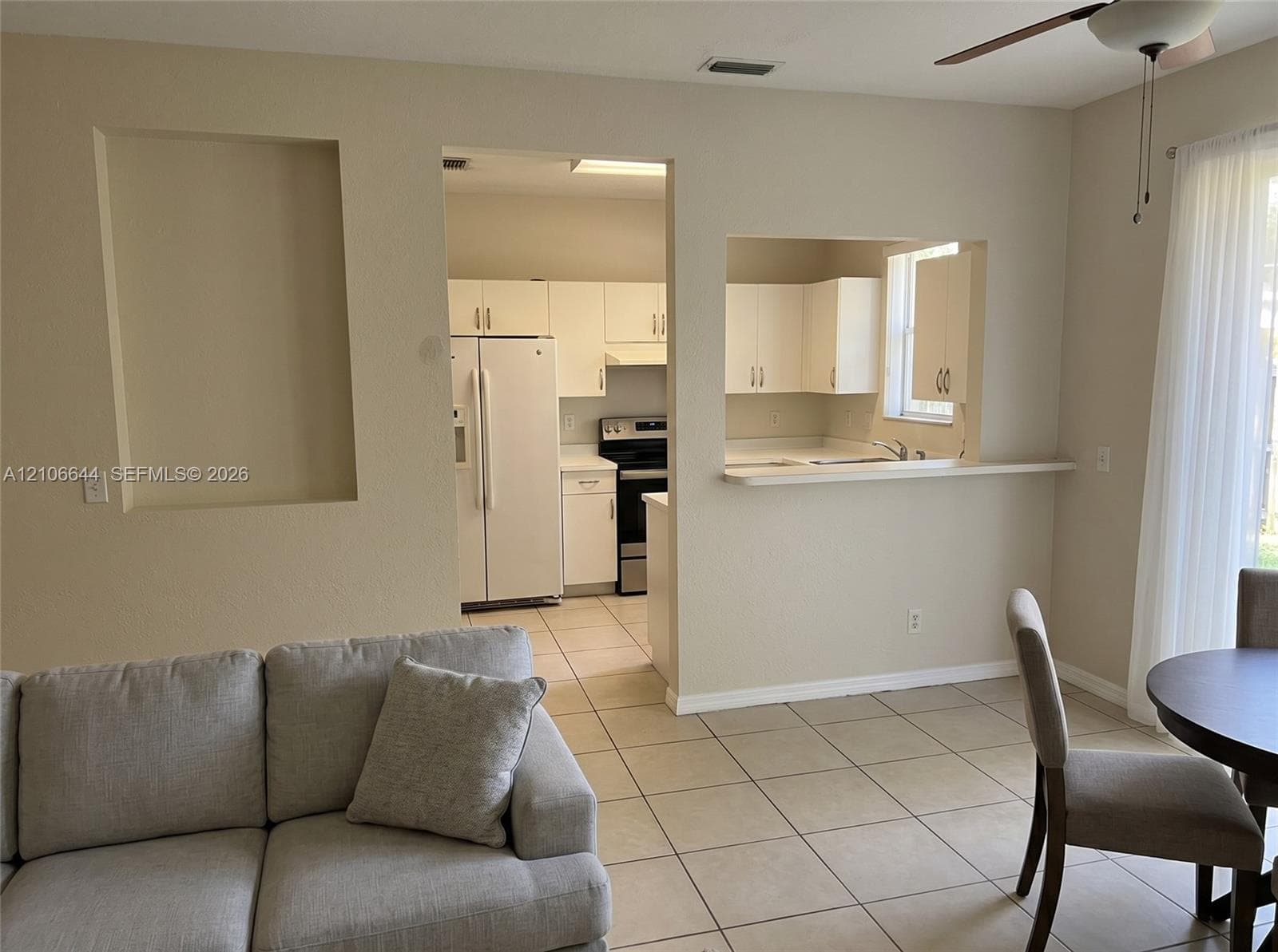 Kitchen area featuring white cabinetry, a pass-through window with a ledge, neutral tile flooring, and a recessed wall niche