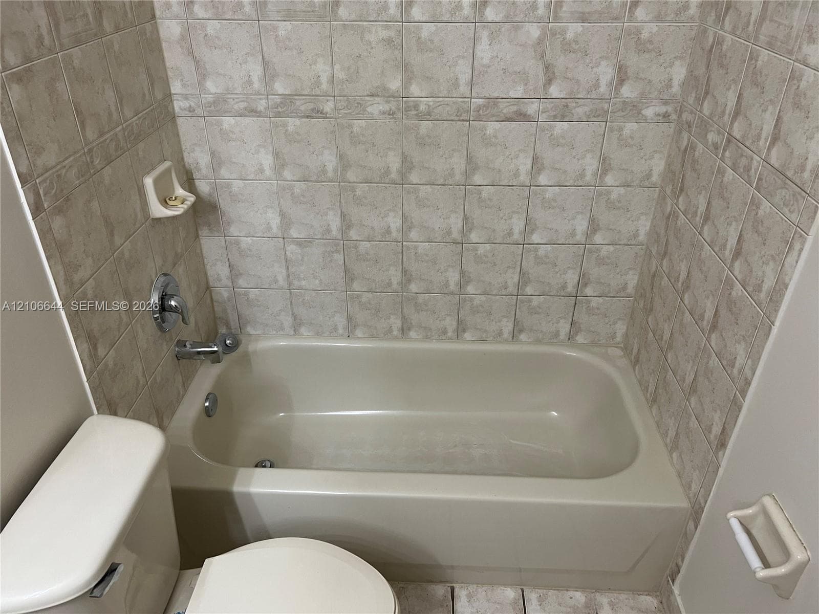 Bathtub surround featuring neutral-toned tile, built-in soap dish, and polished chrome faucet and shower hardware