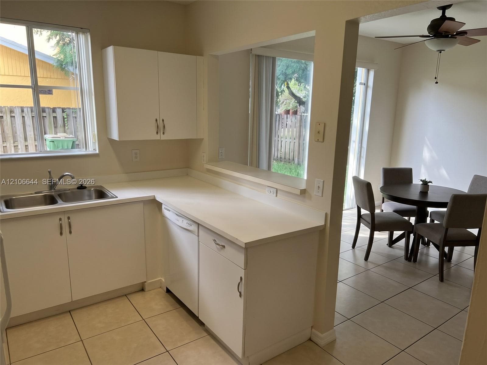 Kitchen featuring white cabinetry, solid surface countertops, stainless steel double-basin sink, and ceramic tile flooring