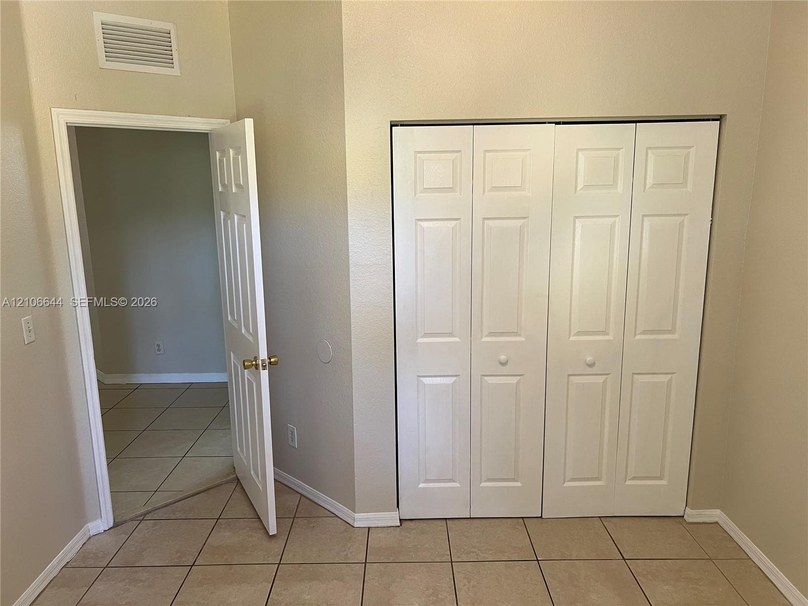 Ceramic tile flooring, white bi-fold closet doors, and interior door with brass-finish hardware