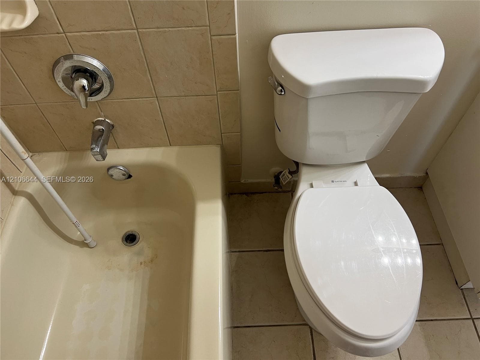 Bathroom featuring a porcelain toilet and a bathtub with a chrome single-handle mixing valve and spout, accented by tiled wall surrounds and floor tiling