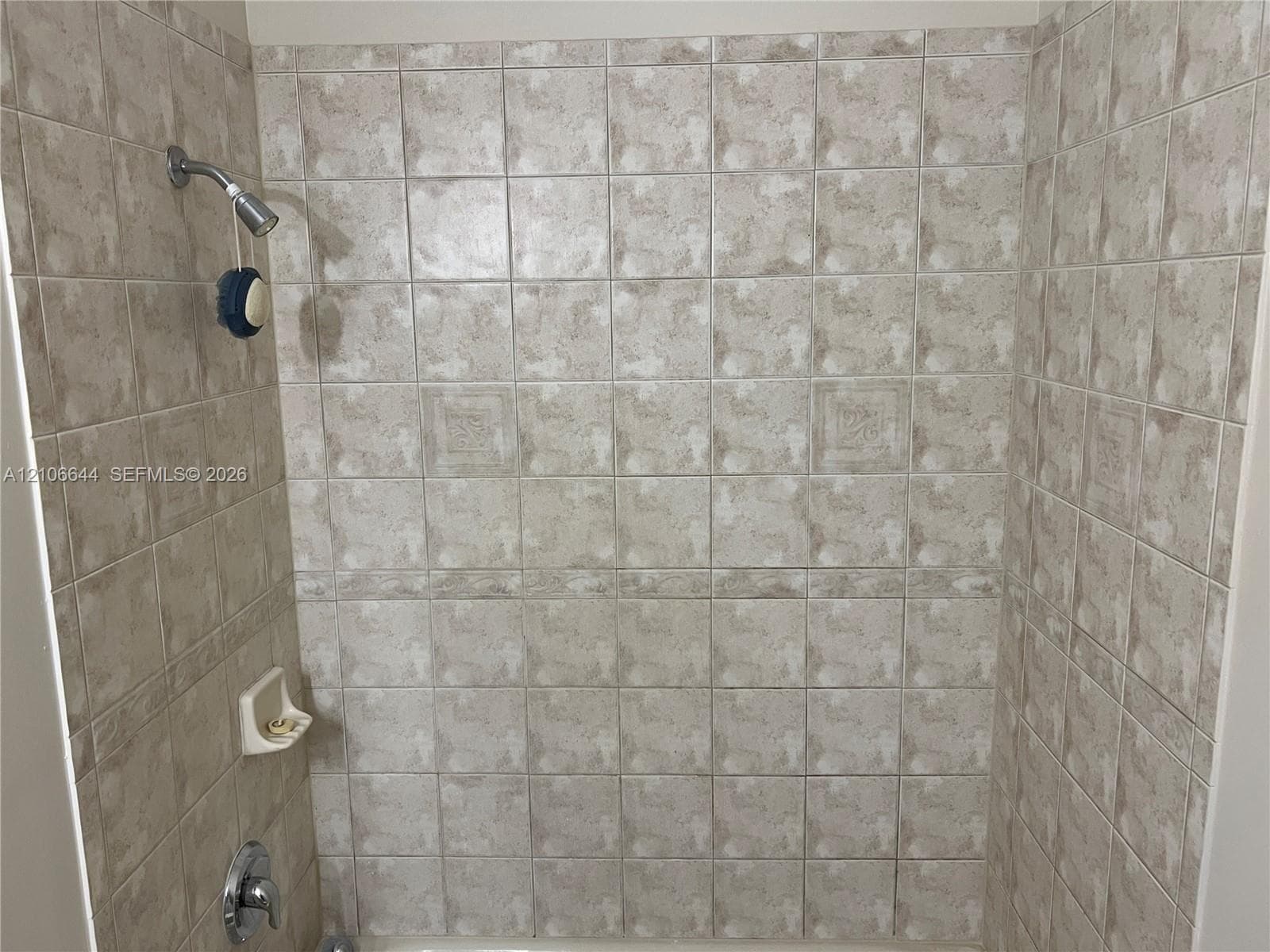 Full-height tiled shower surround featuring neutral-toned stone-patterned tiles, decorative inlay detailing, a built-in recessed soap niche, and a wall-mounted showerhead with single-handle mixing valve