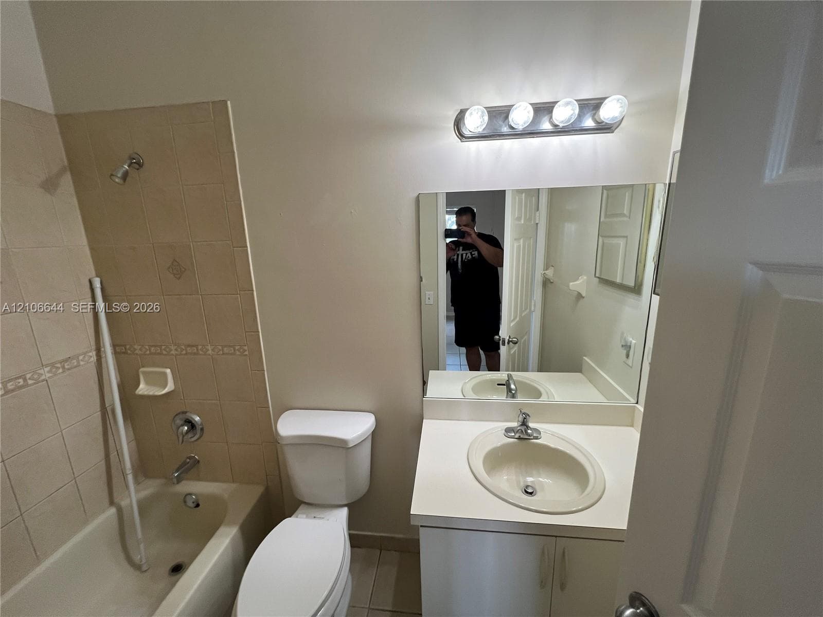 Bathroom featuring a vanity with a solid-surface countertop, an integrated sink, a tiled tub surround, and a four-light fixture above a wall-mounted mirror