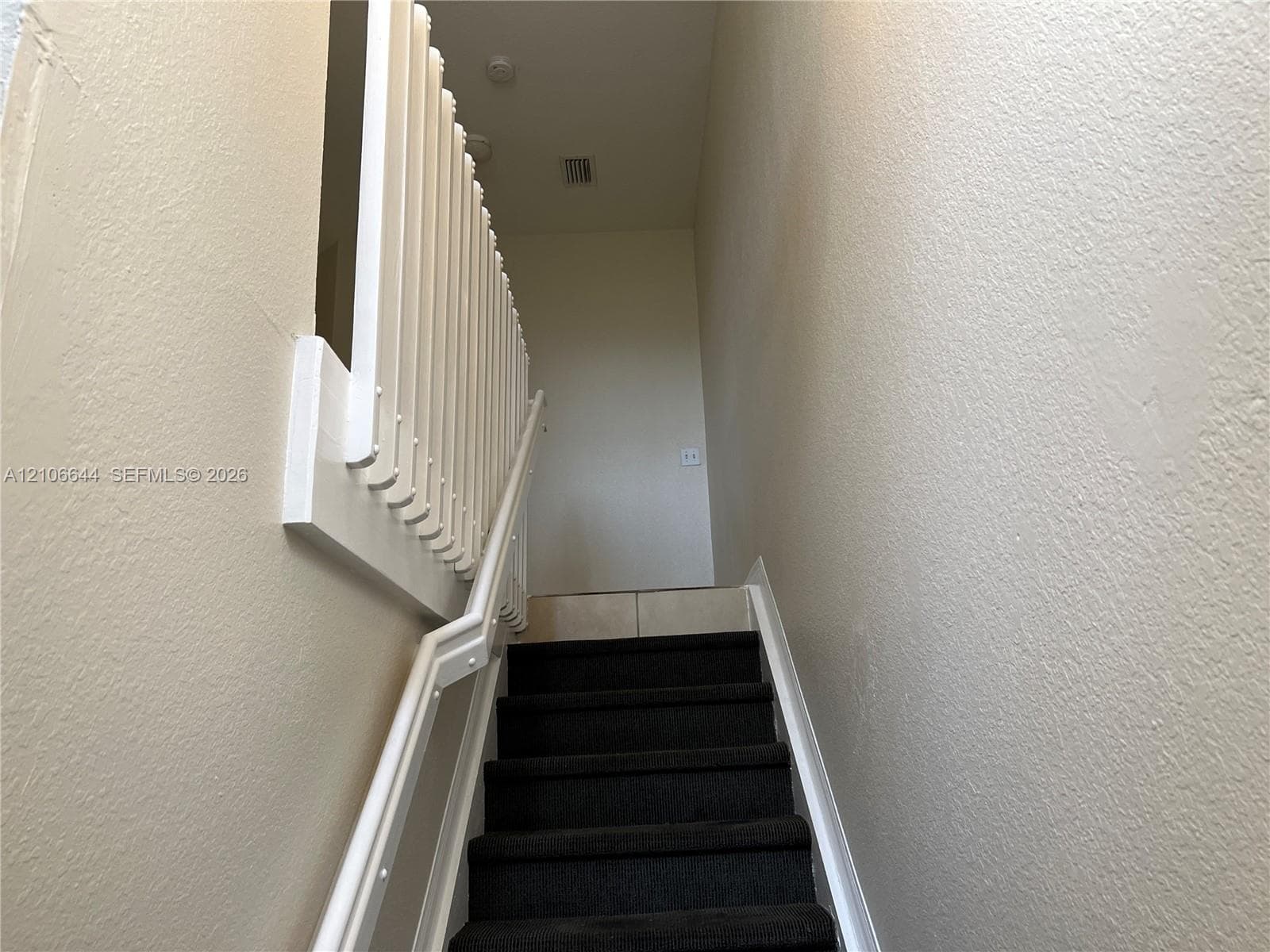 Staircase featuring dark carpeted treads and white painted vertical balustrades with a matching handrail