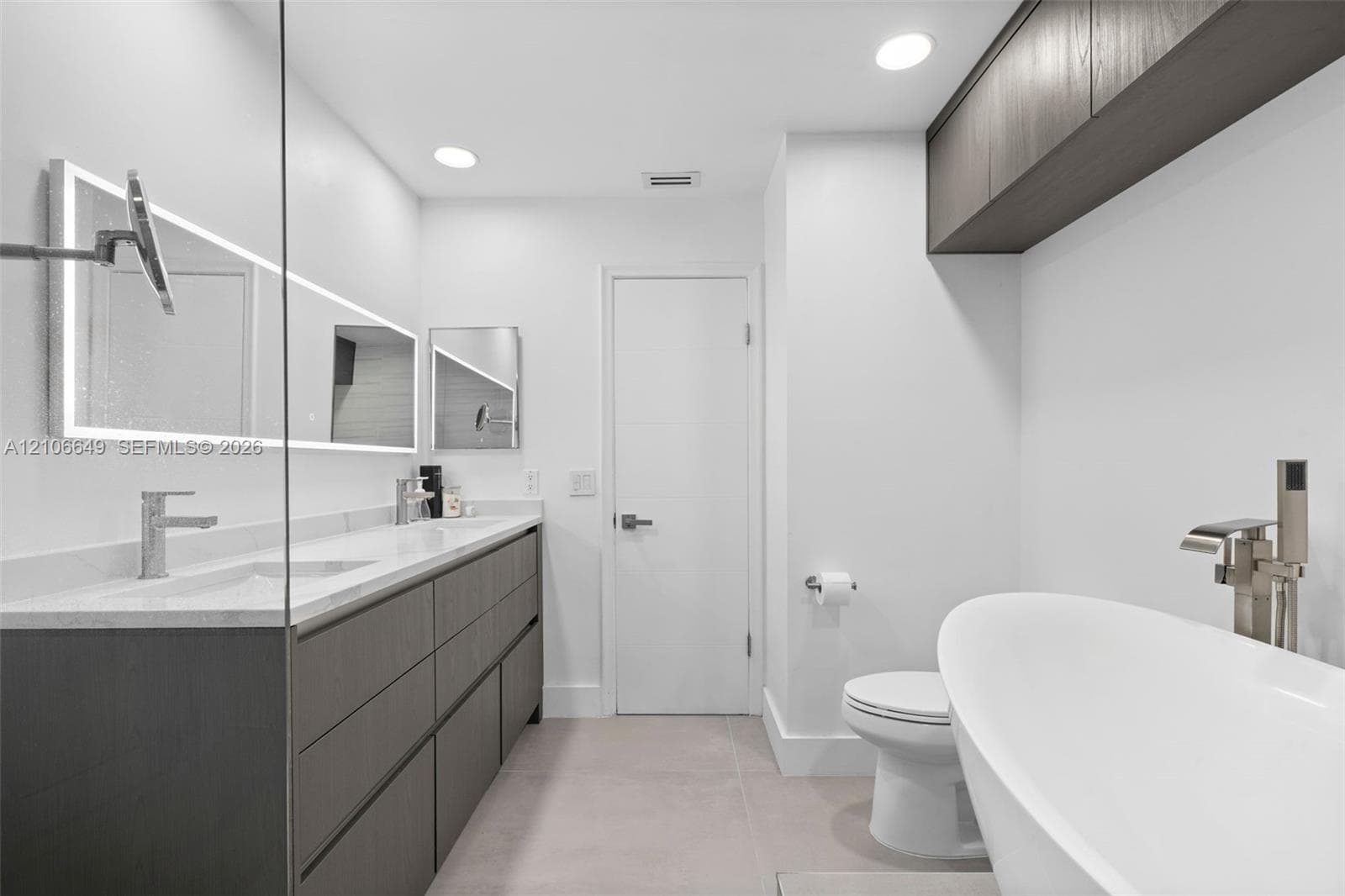 Modern dual vanity with stone countertop, freestanding soaking tub, wall-mounted faucets, and dark wood-finish cabinetry