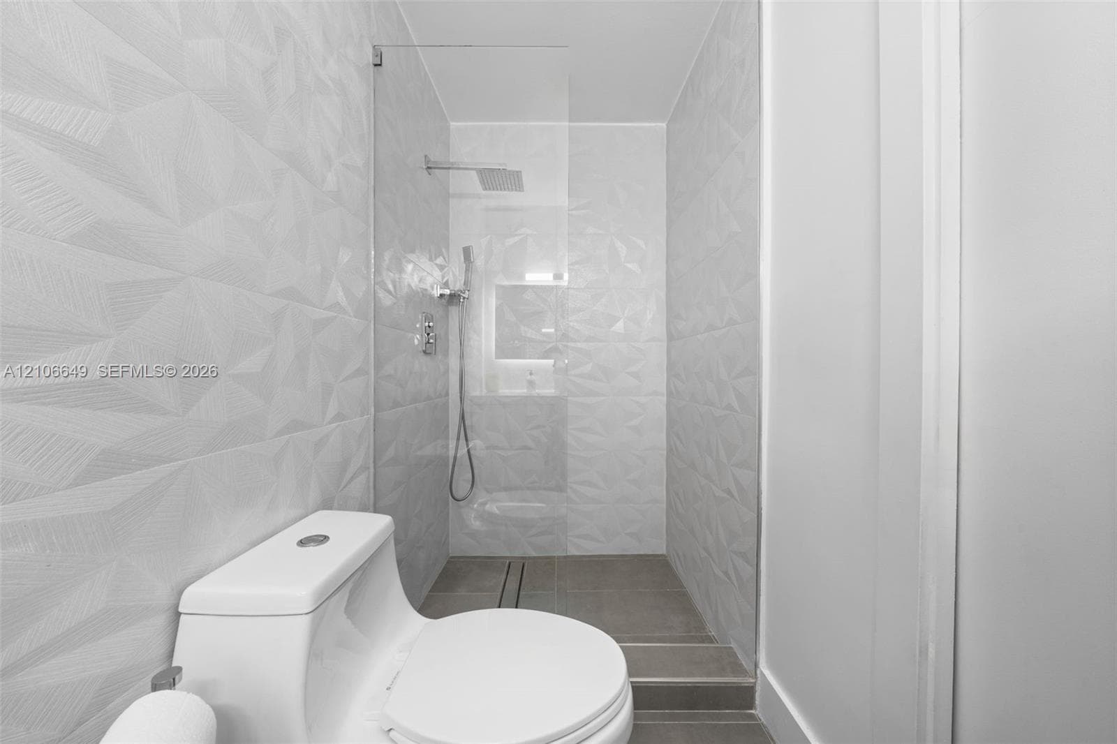 Walk-in shower featuring textured geometric wall tile, a frameless glass enclosure, a rainfall showerhead, and a built-in recessed niche