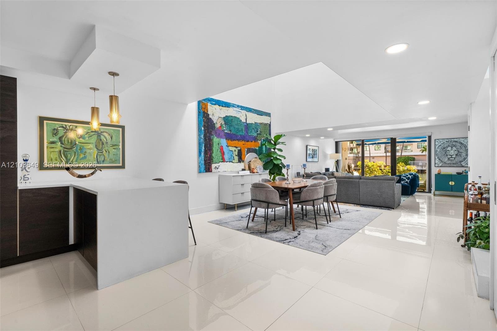 Open-concept living space featuring white polished tile flooring, recessed ceiling lighting, a waterfall-edge kitchen island, dual pendant lights, and large sliding glass doors