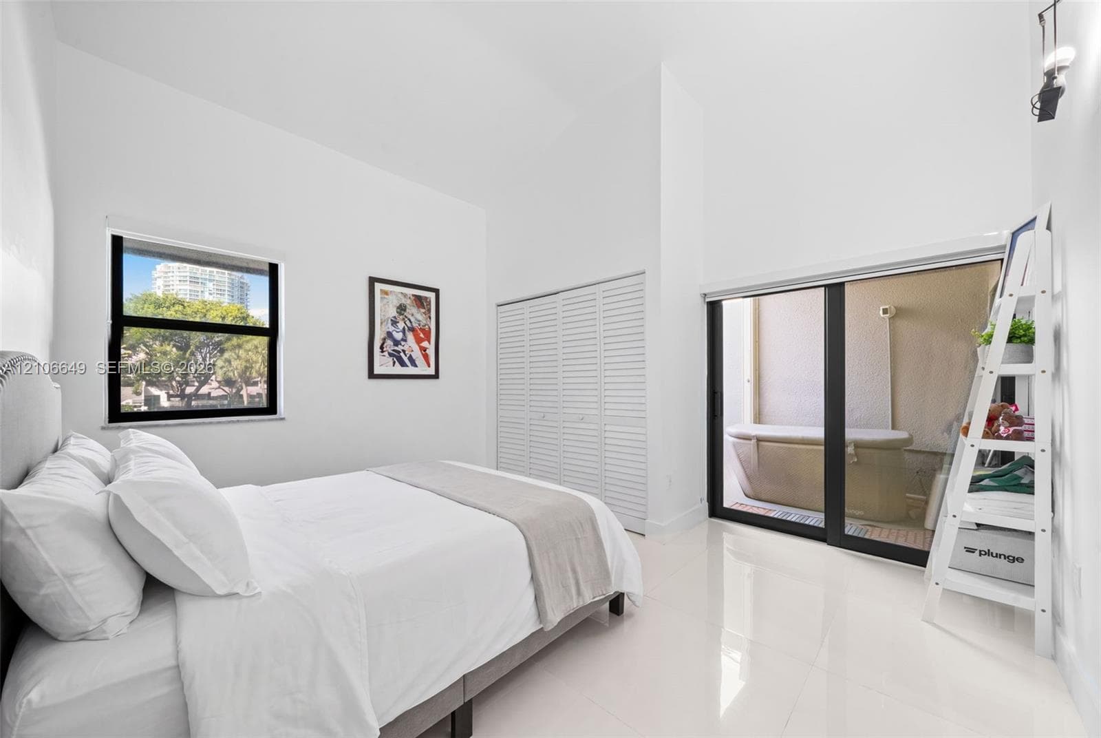 High-ceiling room featuring white tile flooring, louvered-panel closet doors, and a large sliding glass door with access to an exterior area