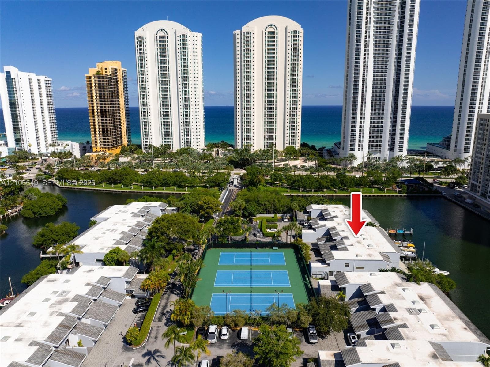 Aerial view featuring a swimming pool with integrated stairs, expansive paved deck, mature palm trees, and perimeter landscaping
