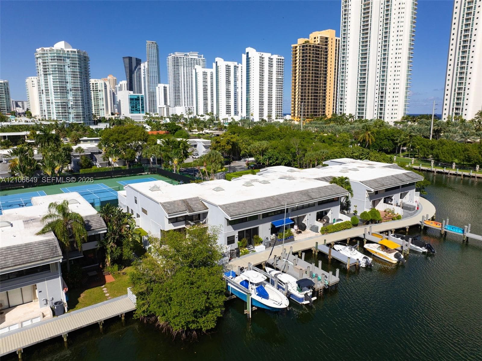 Aerial perspective of a multi-unit property complex featuring tennis courts, a swimming pool, and direct canal access