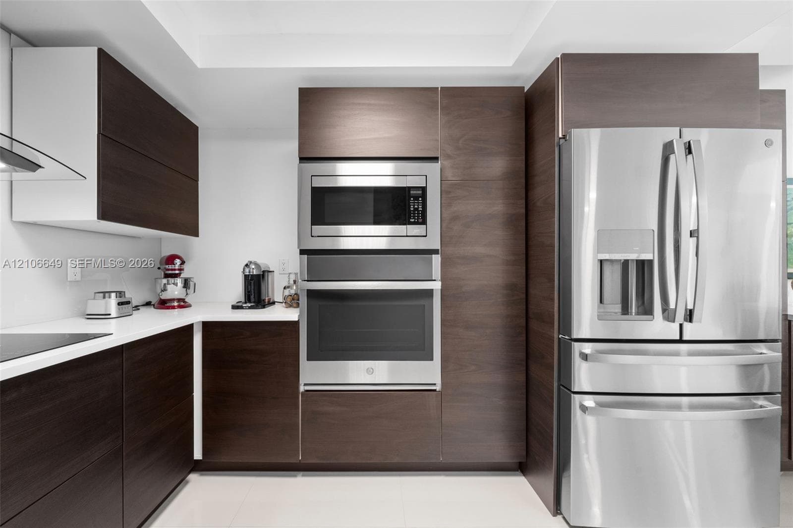 Modern kitchen featuring dark wood-finish cabinetry, solid surface countertops, stainless steel wall oven, built-in microwave, and stainless steel french-door refrigerator