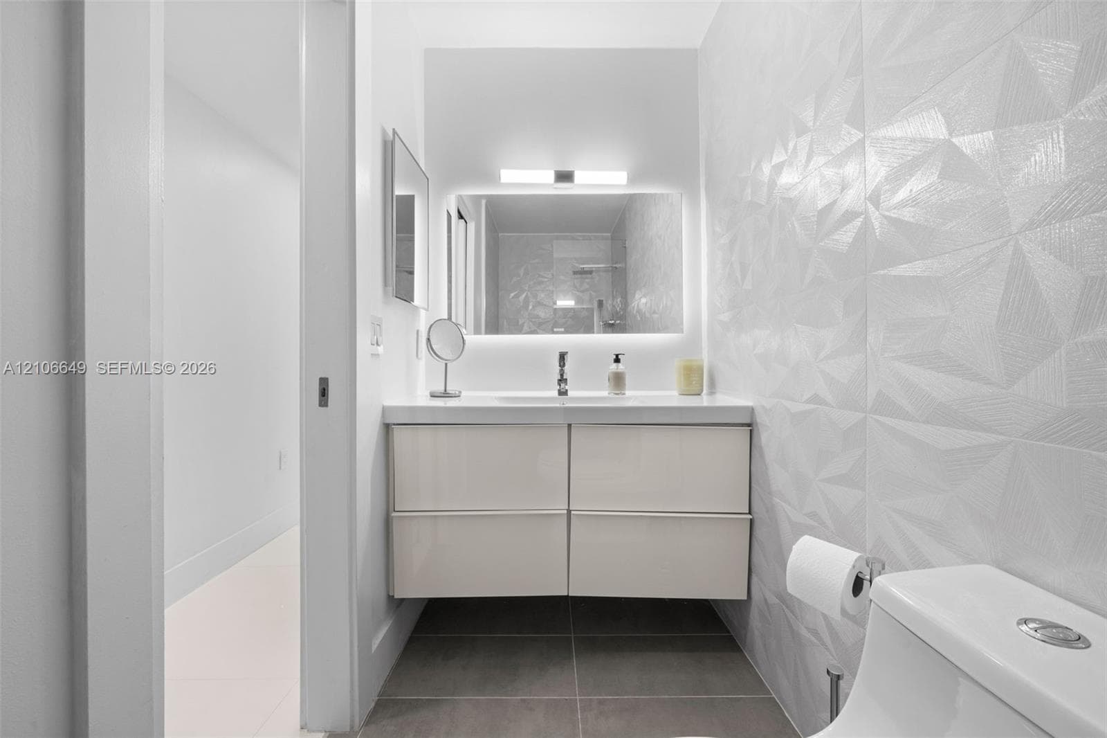 Floating vanity with a smooth-finish countertop, integrated under-mount sink, geometric textured tile walls, and a backlit mirror