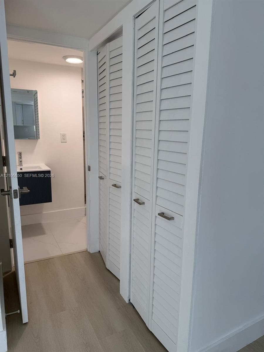 Dual louvered-door closets with brushed metal hardware, wood-finish flooring, and a floating vanity featuring a rectangular sink and matte hardware