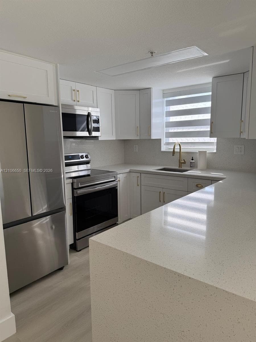 Kitchen featuring white Shaker-style cabinetry, quartz countertops, stainless steel appliances, a metallic faucet, and wood-finish flooring