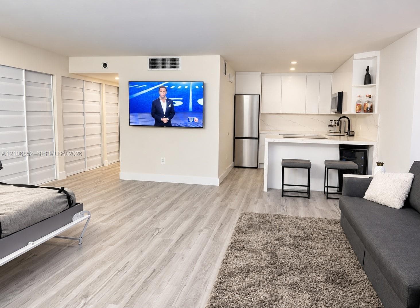 Open-concept kitchen featuring high-gloss white cabinetry, stone countertops, stainless steel appliances, and wood-finish flooring