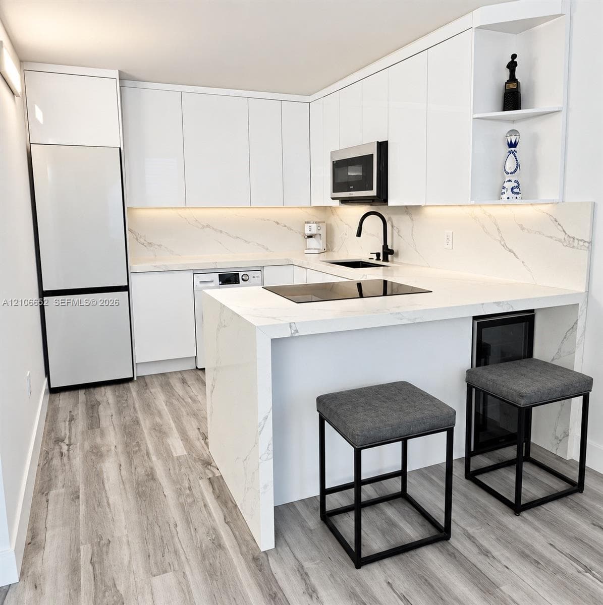 Kitchen featuring high-gloss cabinetry, stone-surface waterfall peninsula, induction cooktop, integrated under-counter beverage refrigerator, and wood-finish flooring