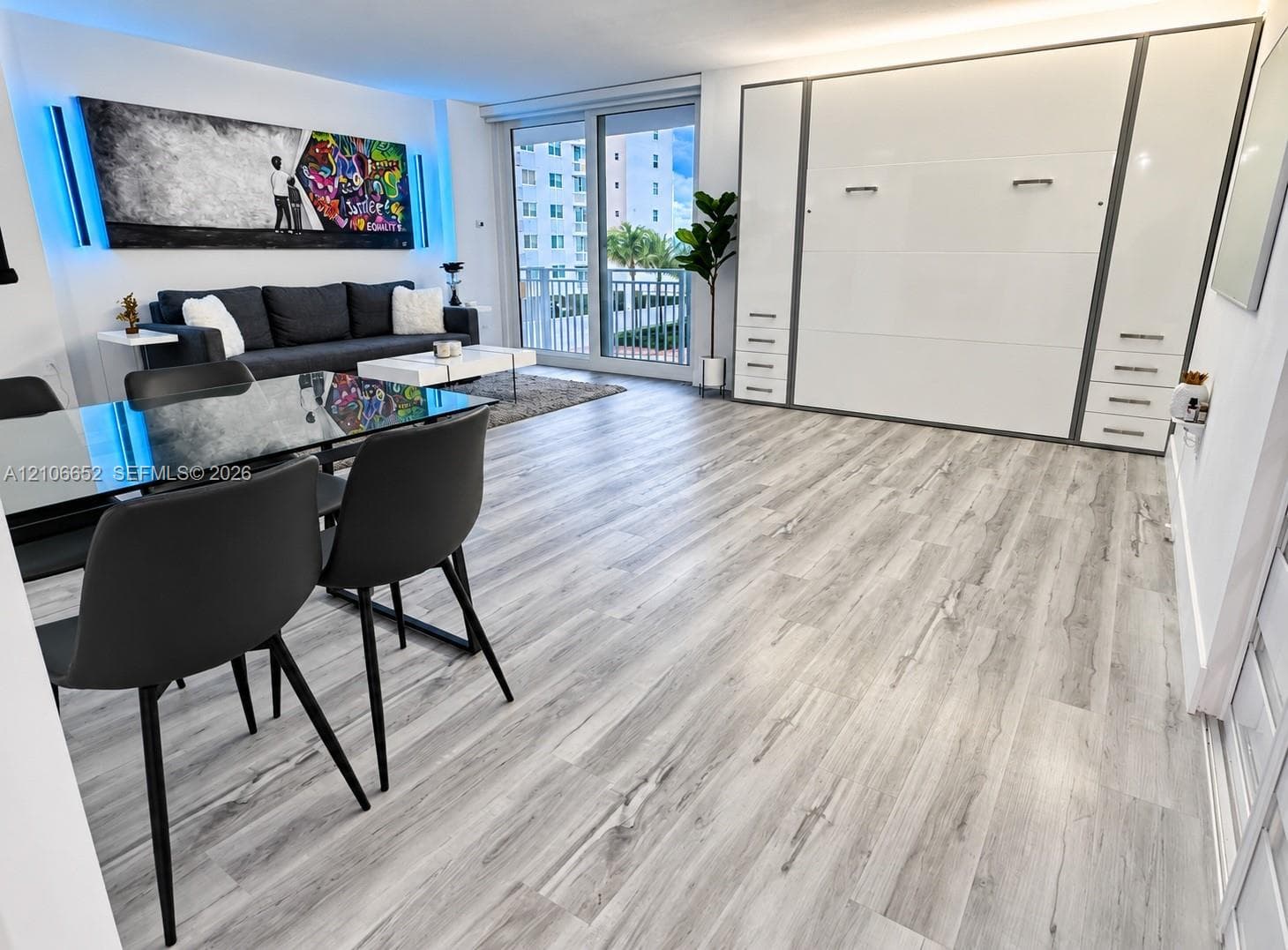 Open-concept living space featuring wood-finish flooring, floor-to-ceiling built-in cabinetry, and a large sliding glass door providing external access to a balcony