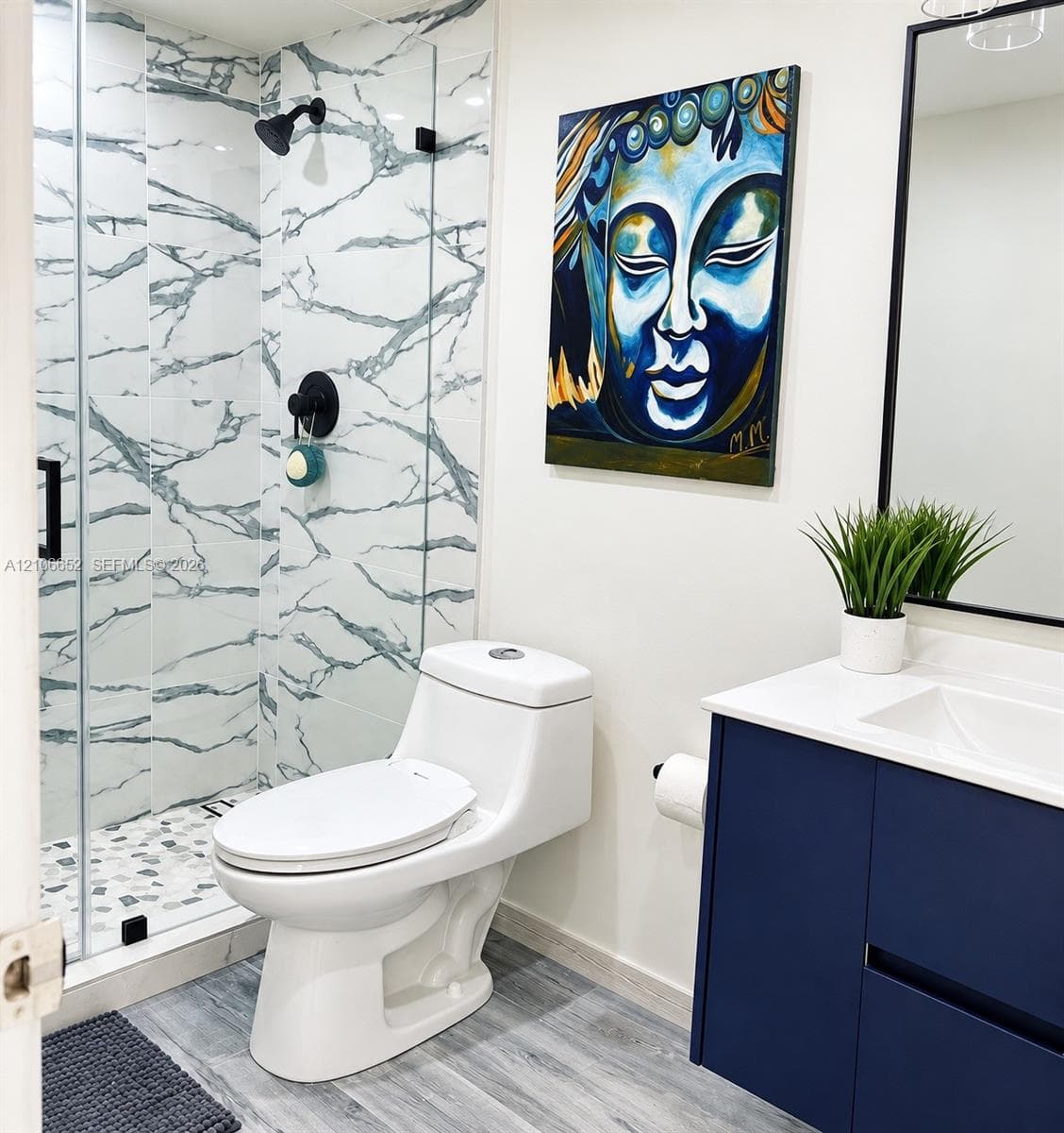 Bathroom featuring a glass-enclosed shower with vein-patterned wall tile and stone-style floor tile, a navy blue vanity cabinet with a white countertop, and a matte black framed mirror