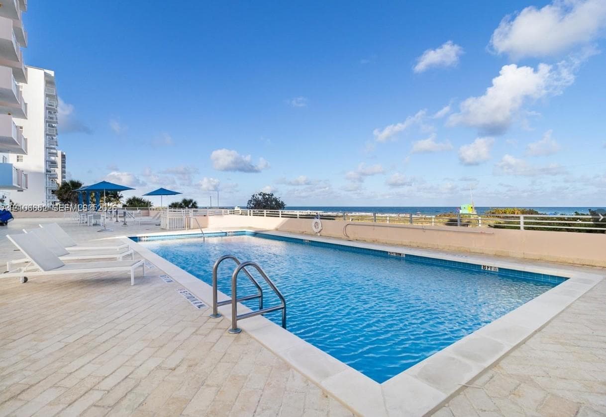 Rectangular swimming pool featuring a metal ladder, light-toned stone paver decking, and a perimeter safety railing