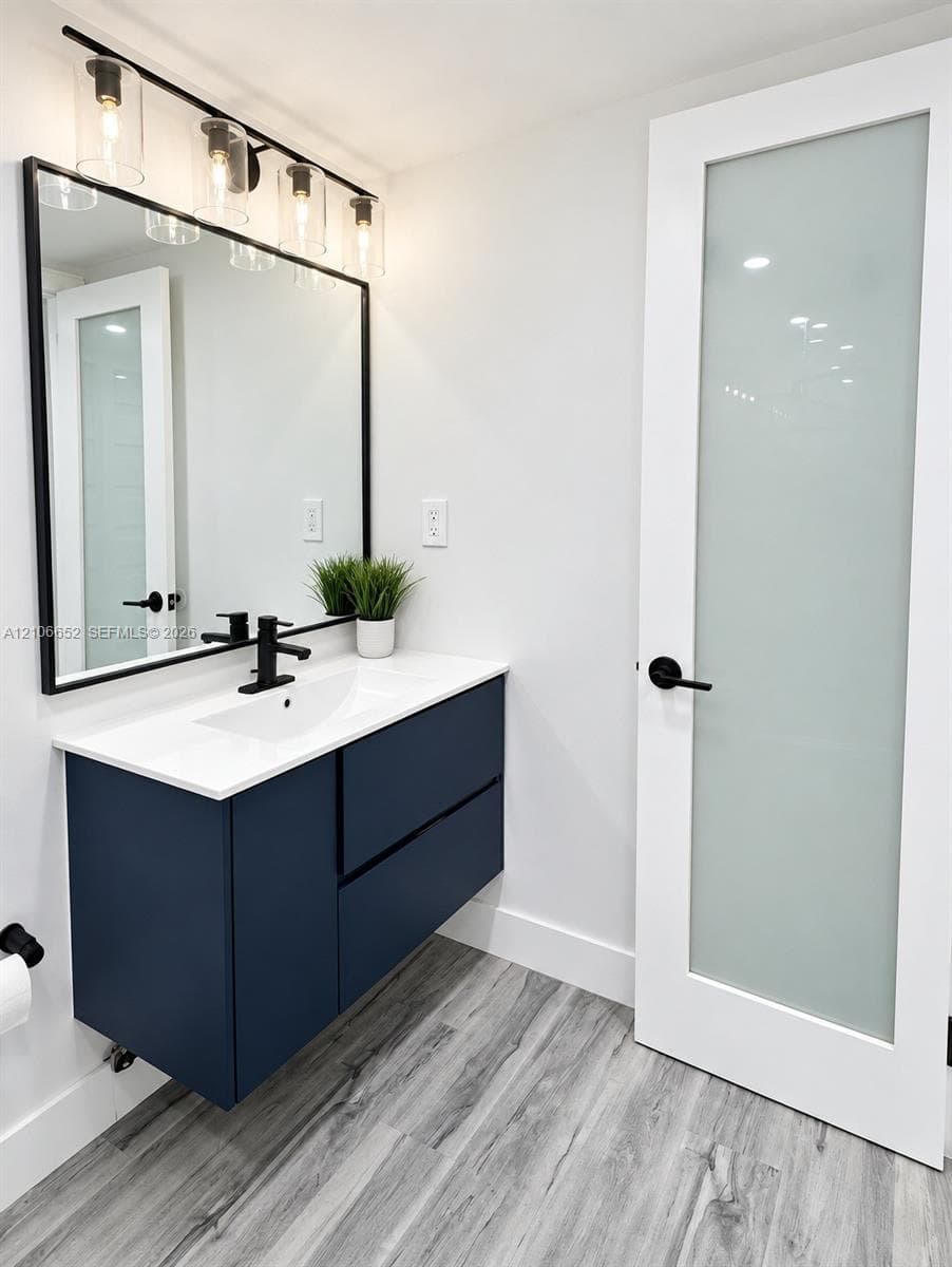 Floating vanity featuring deep blue cabinetry, white countertop with integrated sink, matte black hardware, and wood-finish flooring
