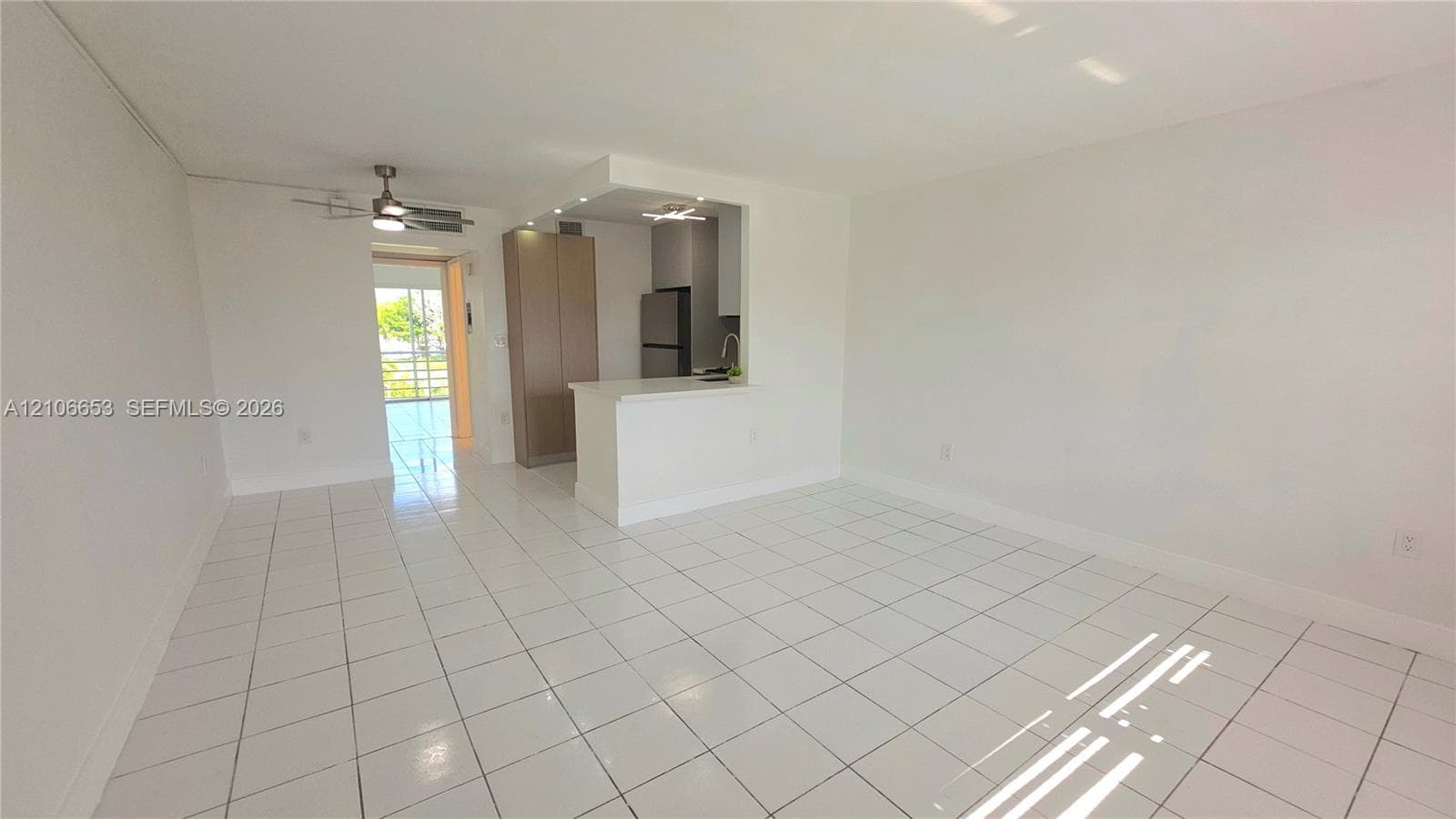 Open-concept interior featuring white ceramic tile flooring, kitchen peninsula with built-in cabinetry, recessed and ceiling fan lighting, and stainless steel kitchen appliances