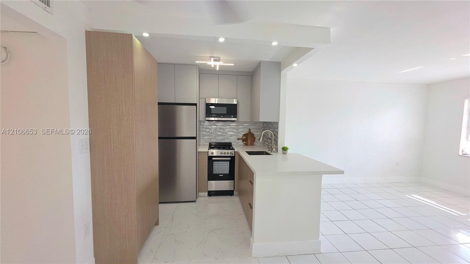Kitchen featuring flat-panel cabinetry, a stainless steel gas range and microwave, a stone-finish tile backsplash, and a peninsula with a stone-finish countertop