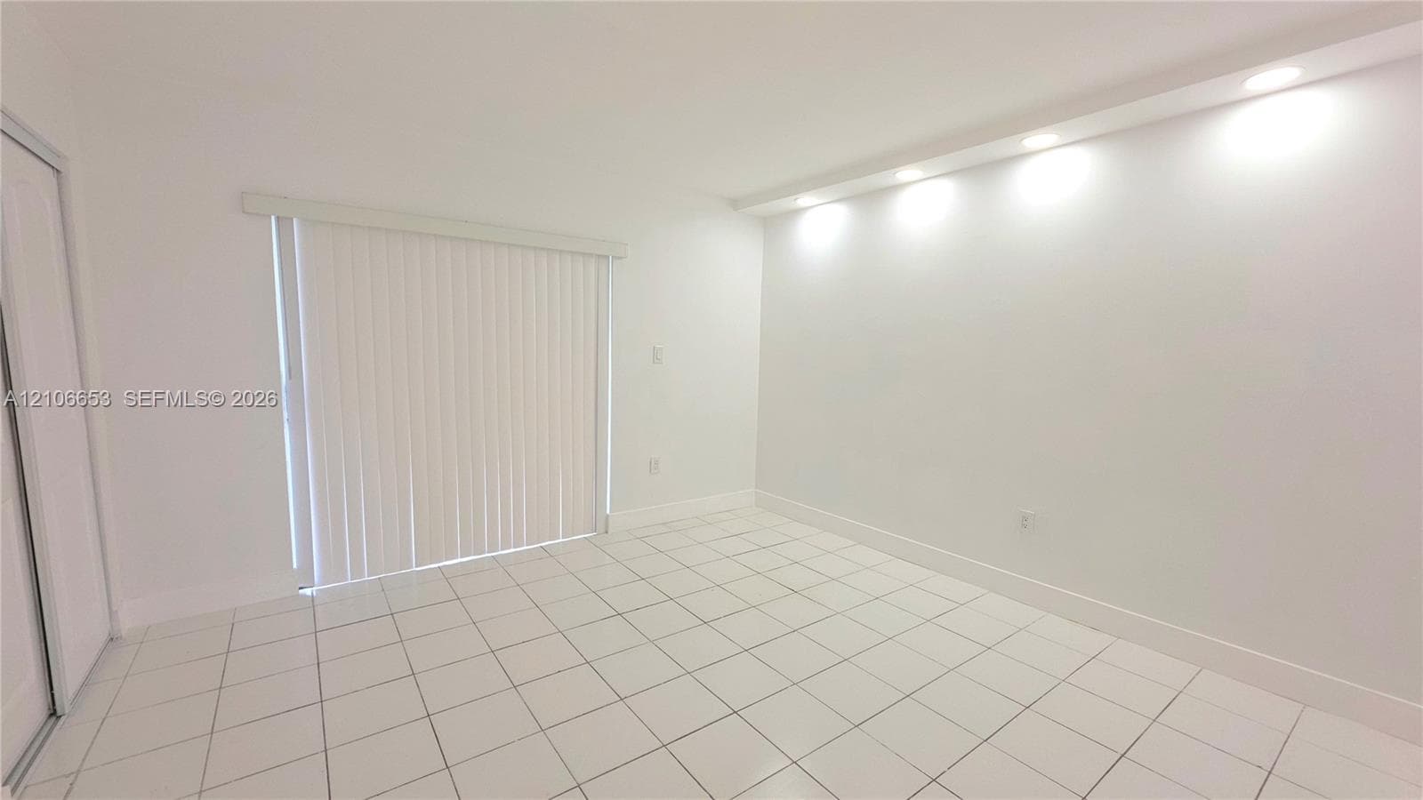 Bright room featuring white ceramic tile flooring, recessed cove lighting, and sliding glass doors with vertical blinds