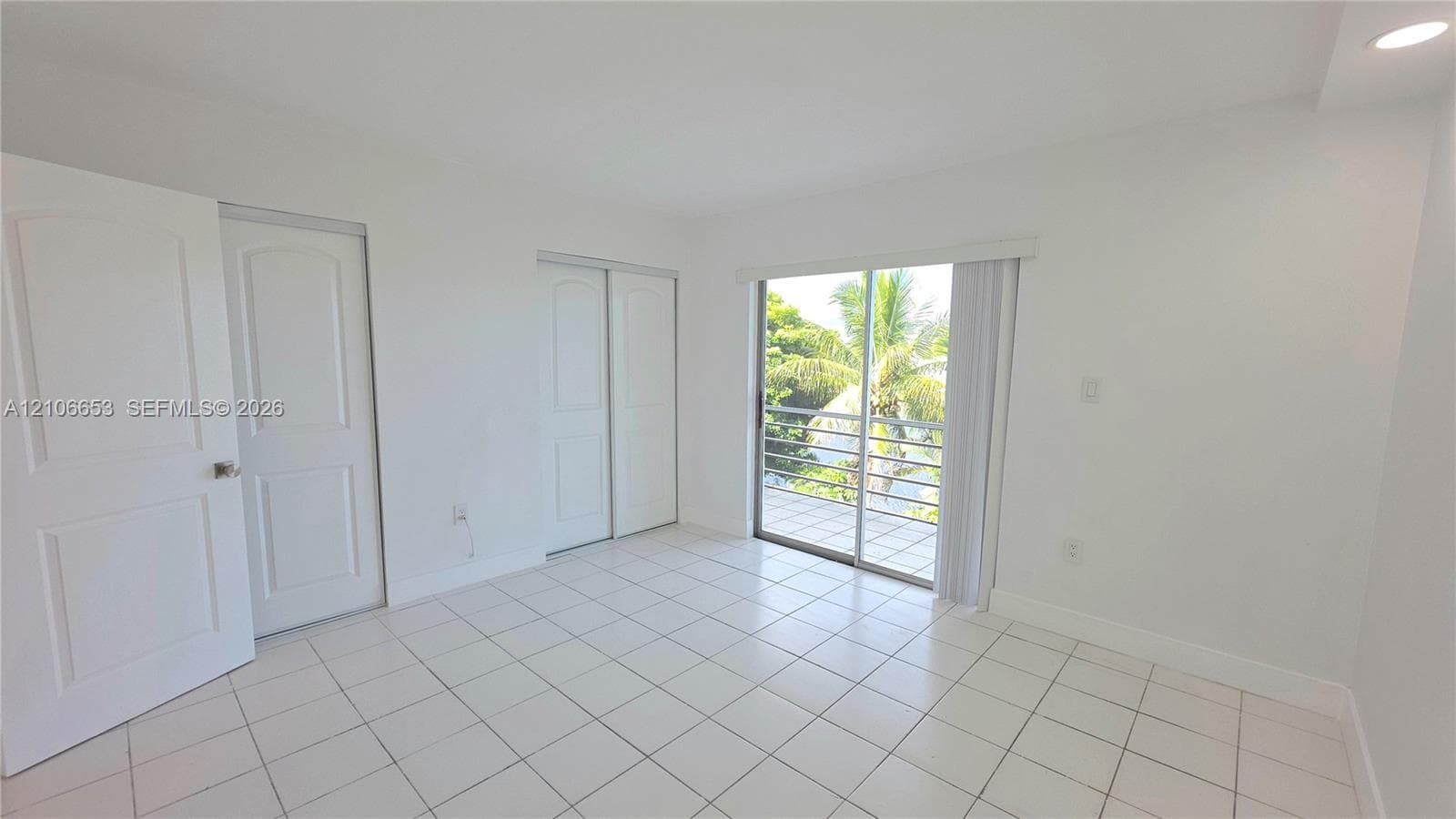 Interior space featuring white tile flooring, recessed ceiling lighting, two-panel interior doors, a sliding glass door, and a built-in closet with sliding doors