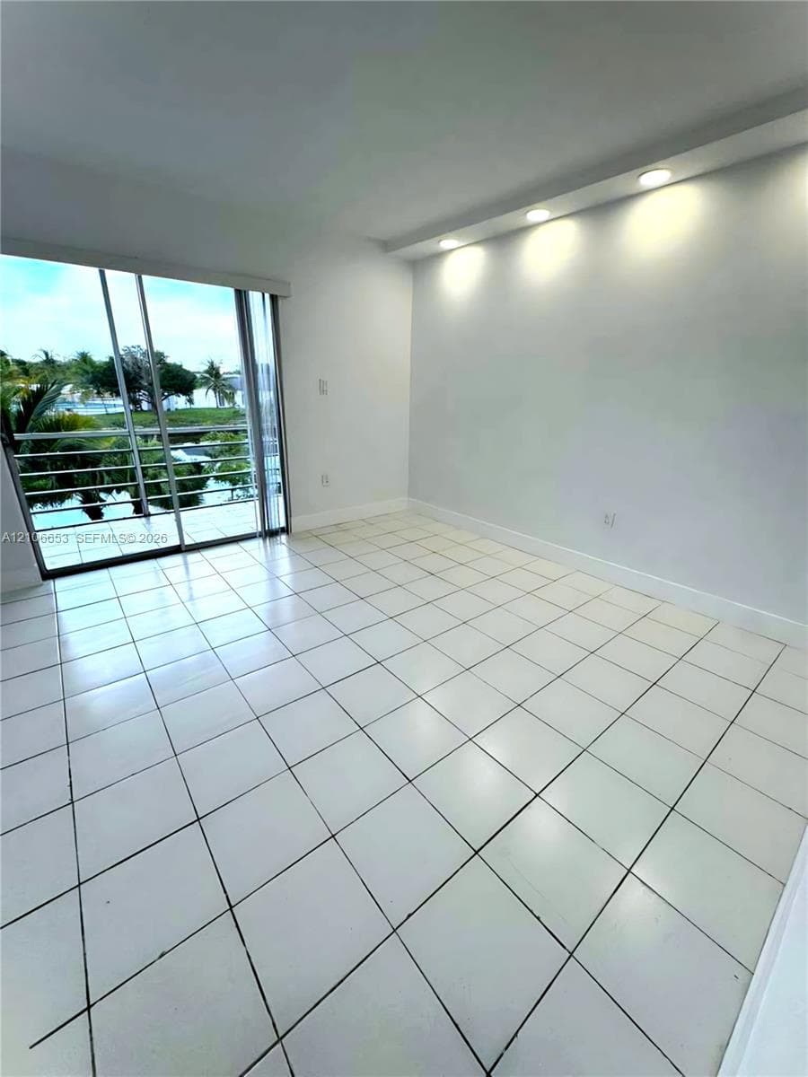 Square tile flooring, recessed soffit lighting, and sliding glass doors opening to a balcony with metal railings and exterior scenery