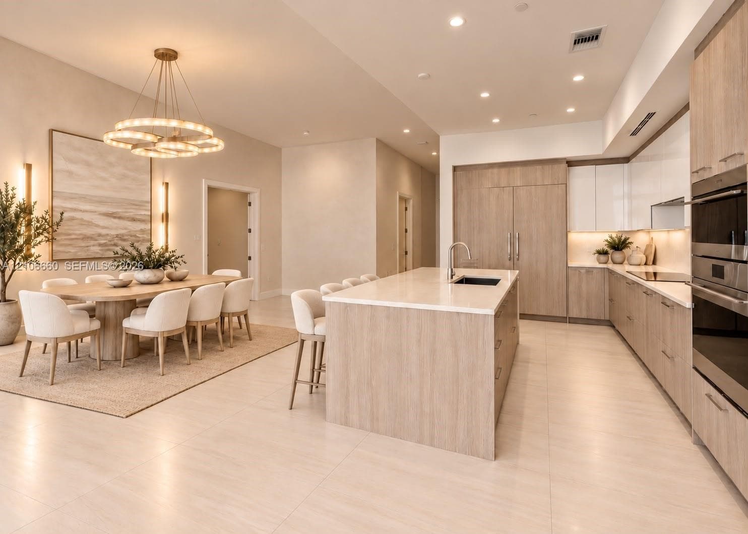 Kitchen featuring light wood-finish cabinetry, a large central island with light-toned countertops, integrated stainless steel appliances, recessed lighting, and a multi-tiered circular chandelier