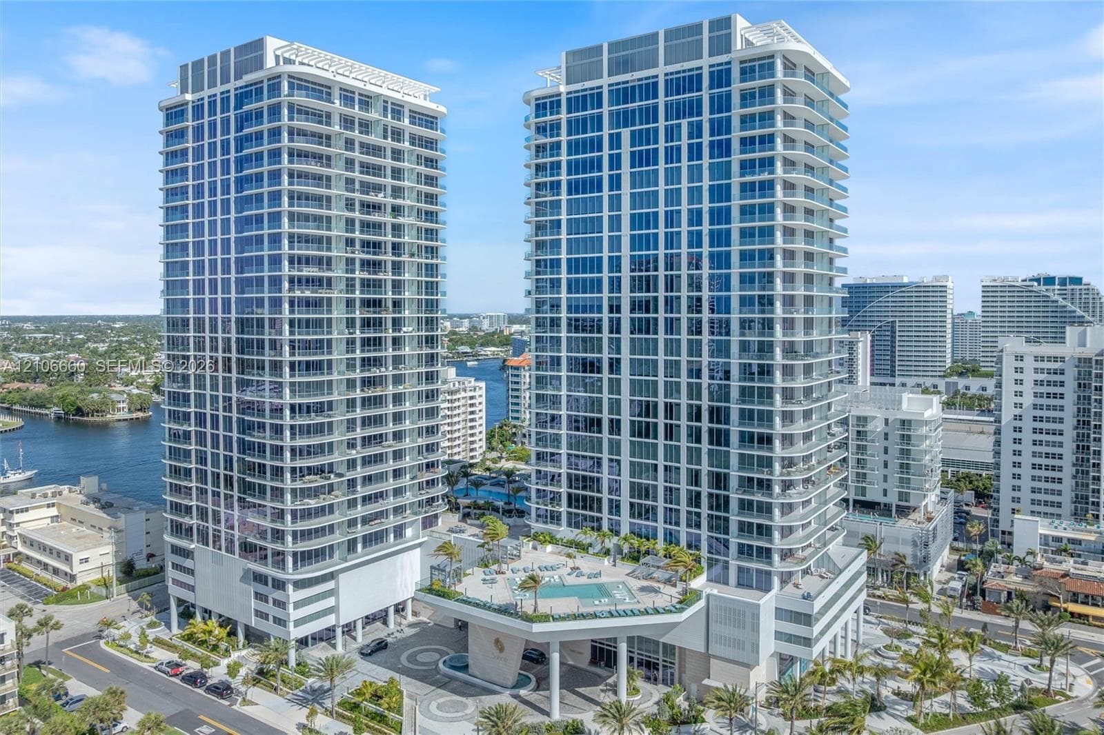 High-rise residential towers featuring floor-to-ceiling glass paneling, wrap-around balconies, an elevated podium pool deck, and structured covered entryway