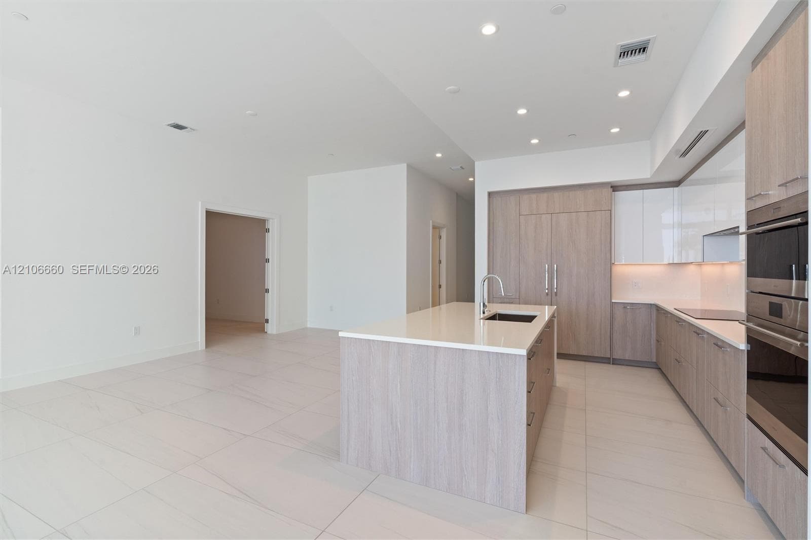 Kitchen featuring wood-finish cabinetry, white high-gloss upper cabinets, solid-surface countertops, large kitchen island with integrated sink, and built-in stainless steel double ovens