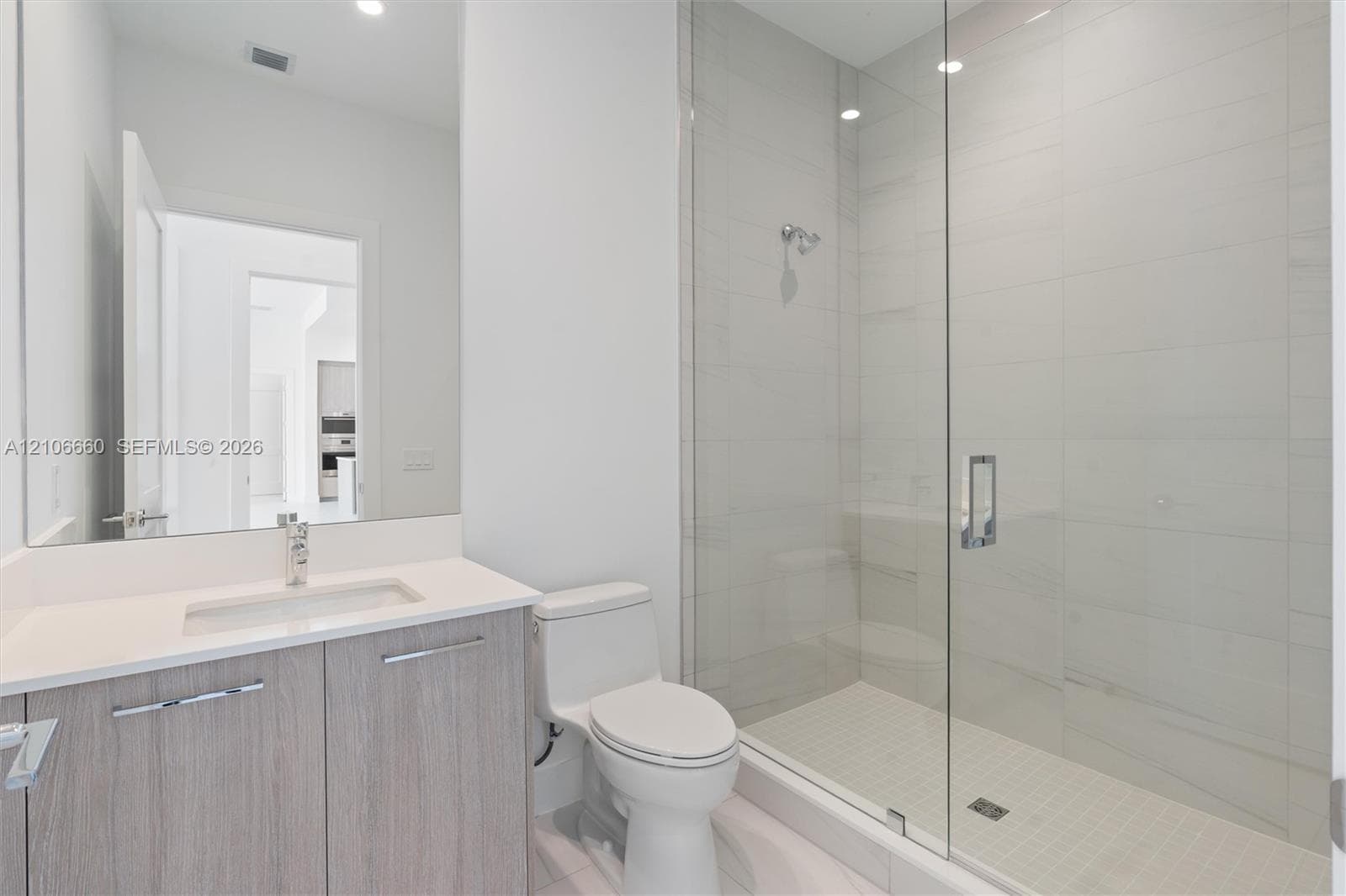 Bathroom featuring a vanity with a white countertop and rectangular undermount sink, a frameless glass-enclosed shower with floor-to-ceiling tile, and chrome fixtures
