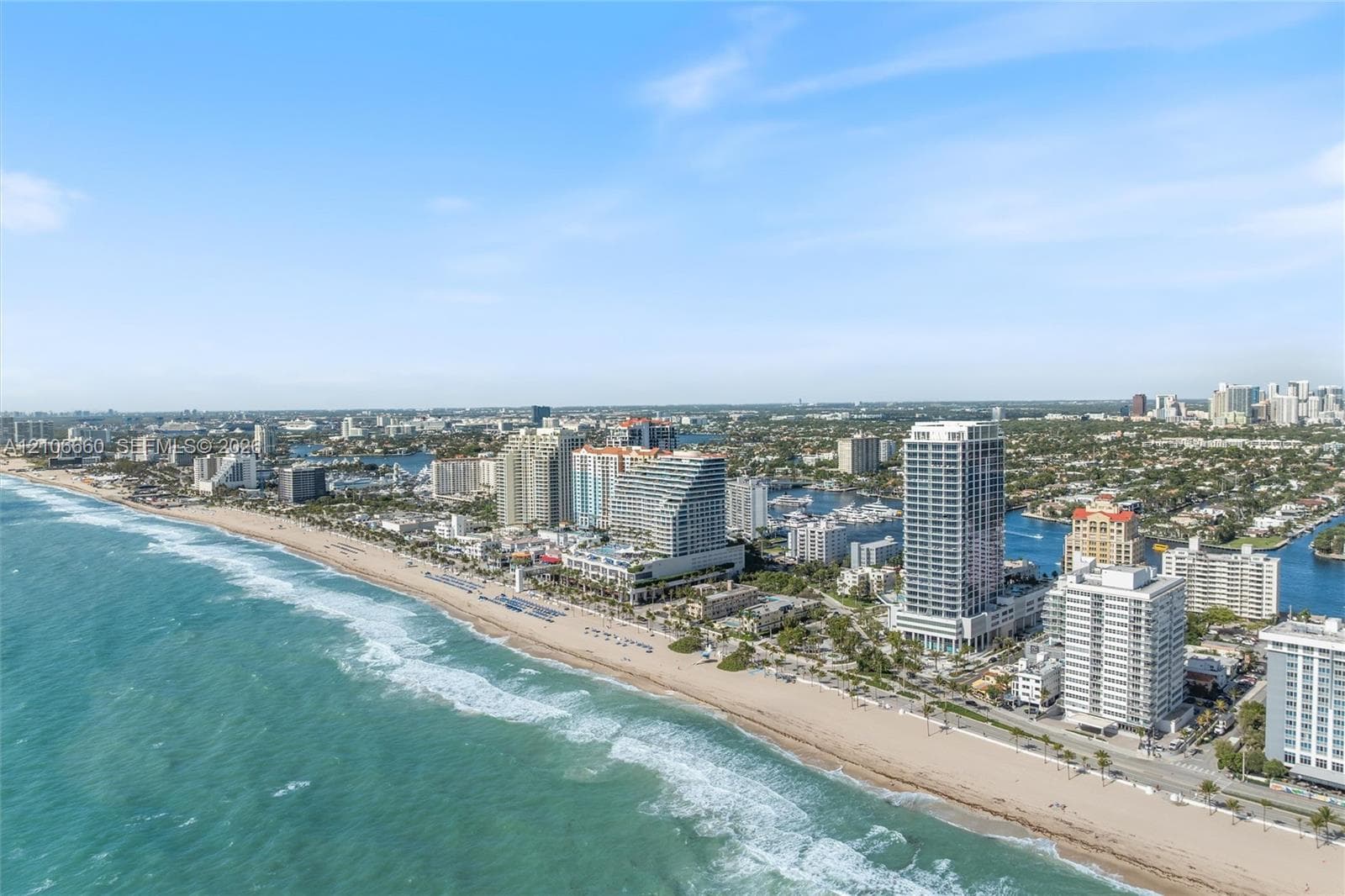 Aerial perspective featuring an extensive stretch of sandy coastline, turquoise ocean waters, and high-density urban development