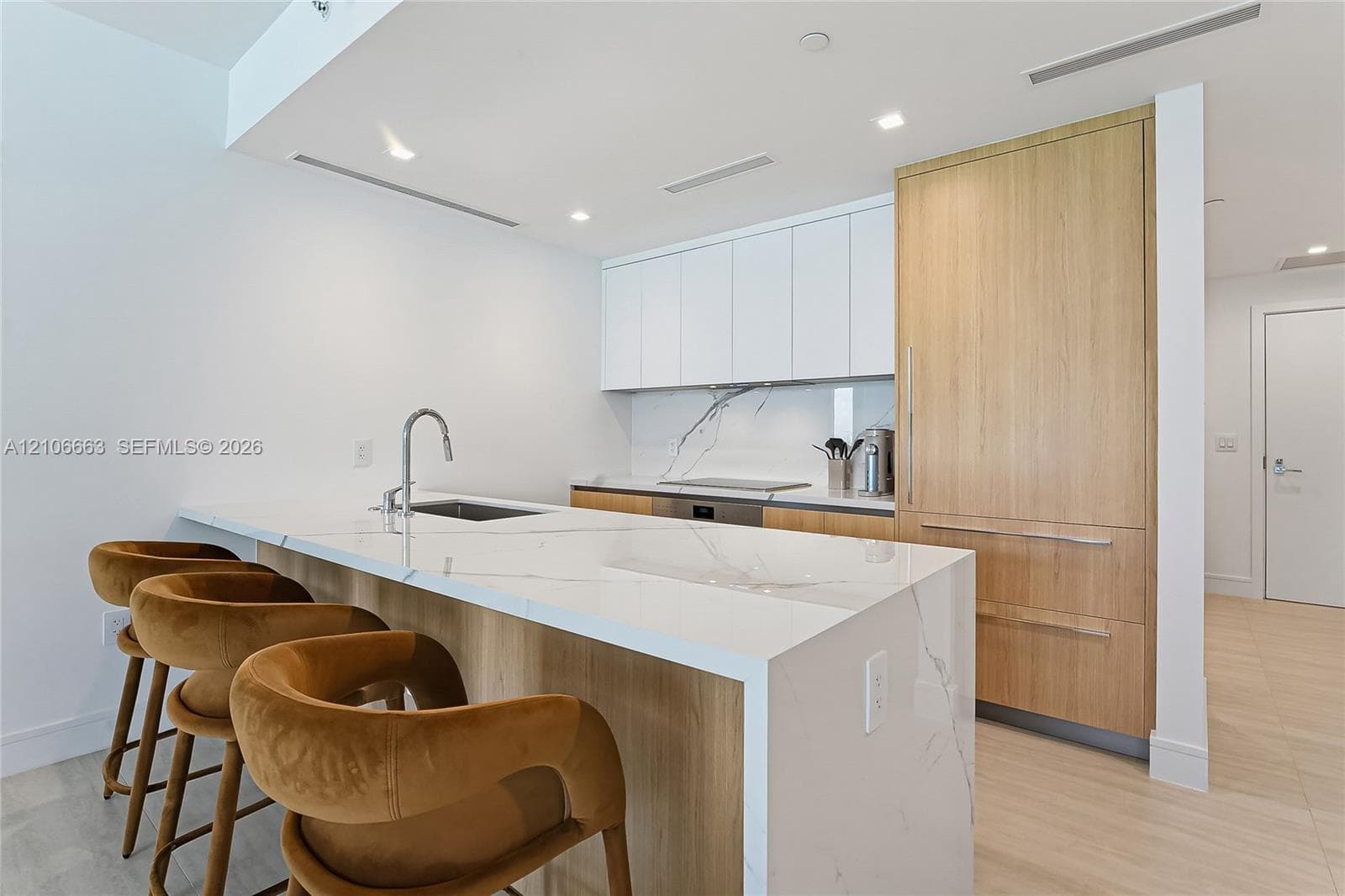 Kitchen featuring waterfall-edge stone countertops, custom cabinetry with wood-finish paneling, integrated refrigerator, stone backsplash, and stainless-steel sink with a gooseneck faucet