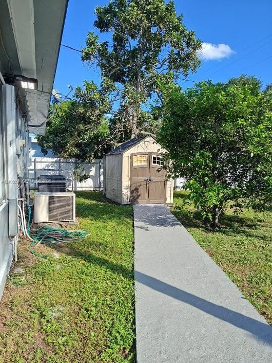 Rear yard featuring a detached storage shed, concrete walkway, white privacy fencing, and mature trees