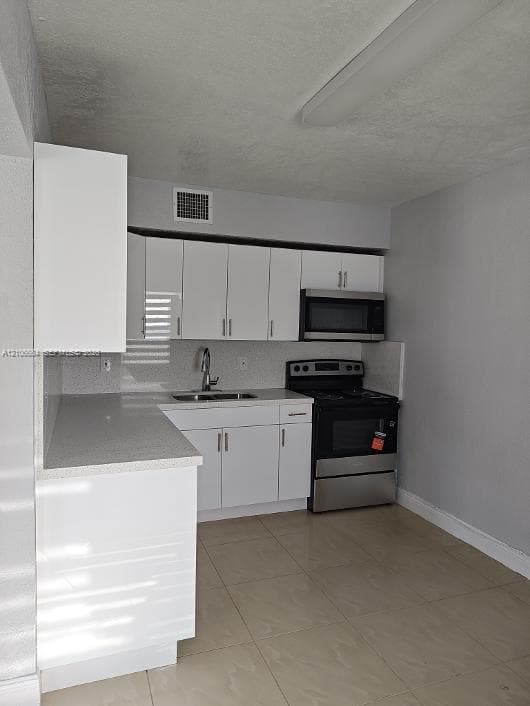 Kitchen featuring white flat-panel cabinetry, stone-finish countertops, stainless steel appliances, a high-arc faucet, and oversized tile flooring