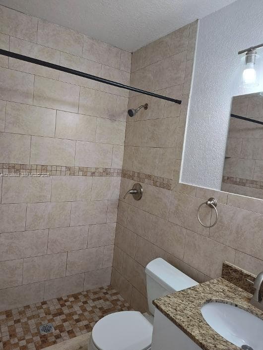 Bathroom featuring a stone-patterned vanity countertop with an integrated undermount sink, shower surround with decorative mosaic tile inlay, and wall-mounted vanity lighting