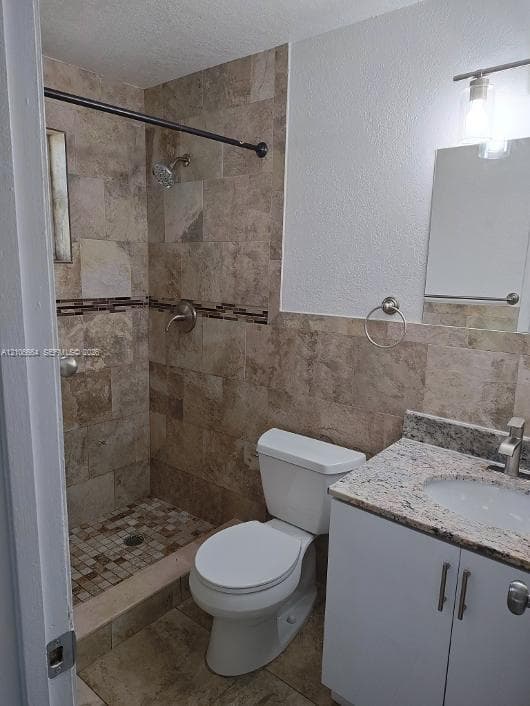 Full bathroom featuring a shower with stone-tile surround and mosaic accent detailing, a stone-composite countertop, vanity cabinetry, and a wall-mounted light fixture