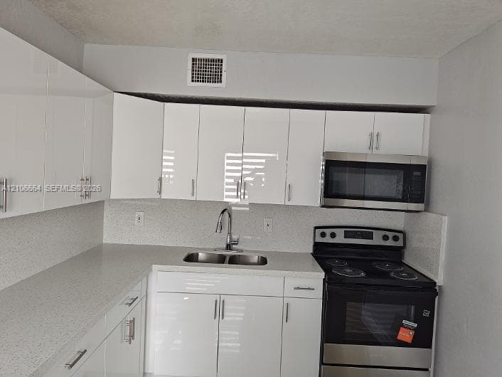 Kitchen featuring white high-gloss cabinetry, stone-finish countertops, dual-basin stainless steel sink, gooseneck faucet, and stainless steel appliances