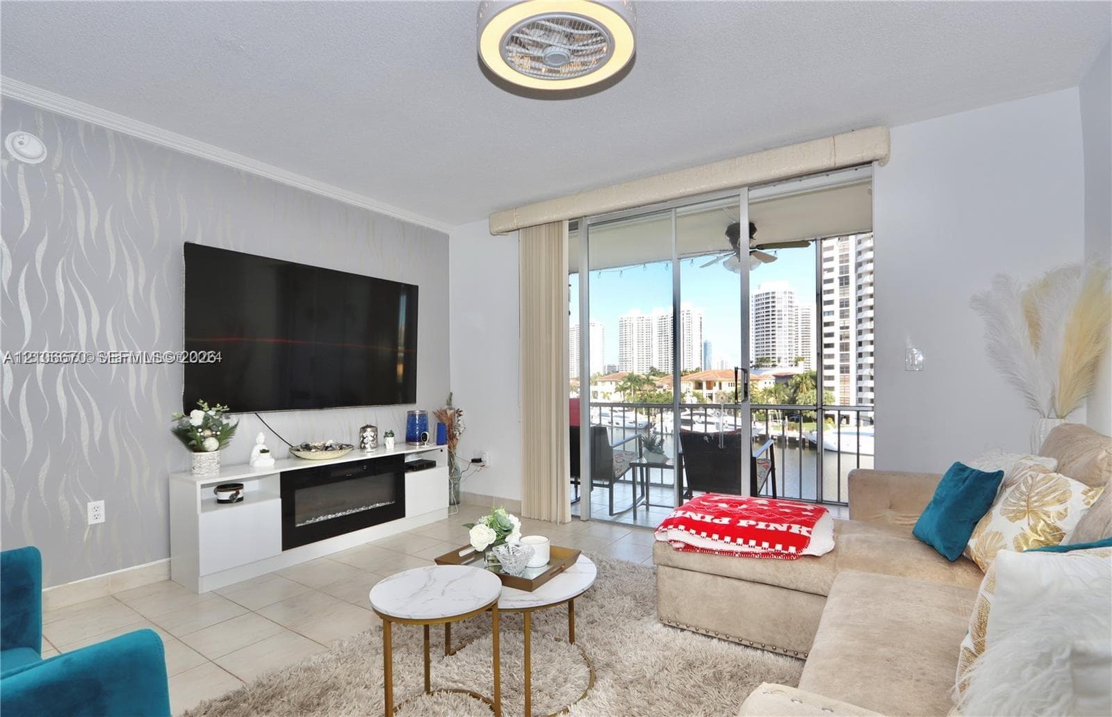 Living area featuring light-toned floor tiles, a floor-to-ceiling accent wall with patterned wallpaper, a built-in media console with an integrated electric fireplace, and sliding glass doors with access to a balcony