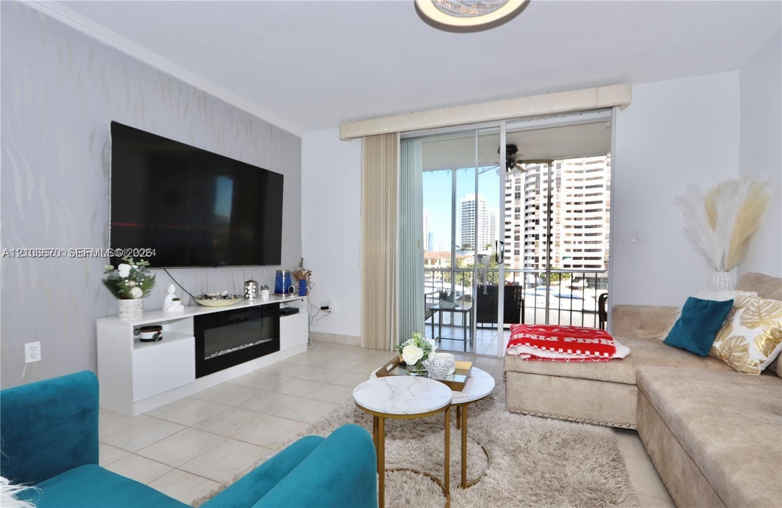 Living area featuring large-format tile flooring, textured accent wall, built-in media console with integrated electric fireplace, and sliding glass doors leading to a balcony
