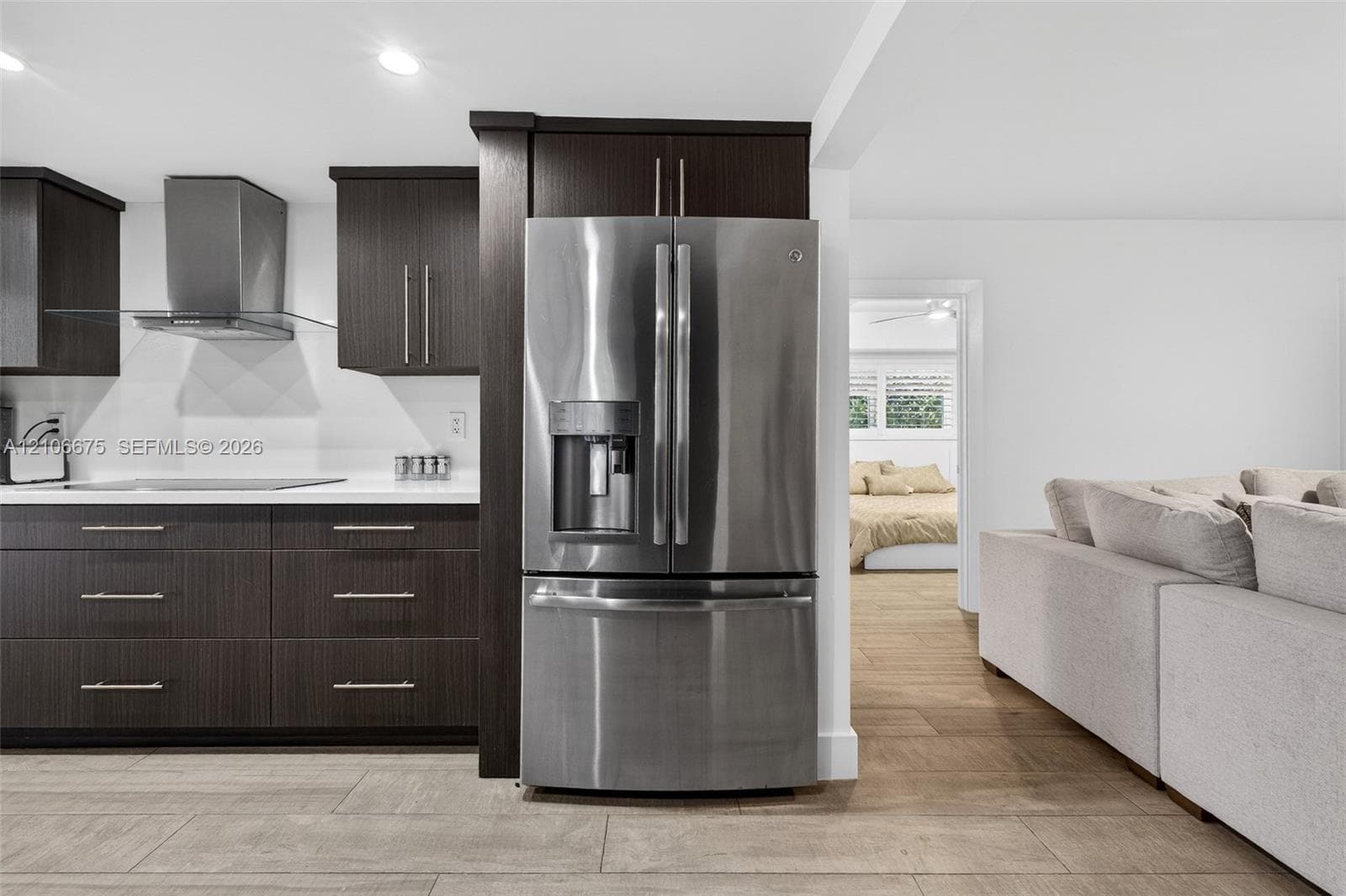 Dark wood-finish cabinetry, stainless steel French-door refrigerator, integrated chimney-style range hood, solid-surface countertops, and wood-finish flooring