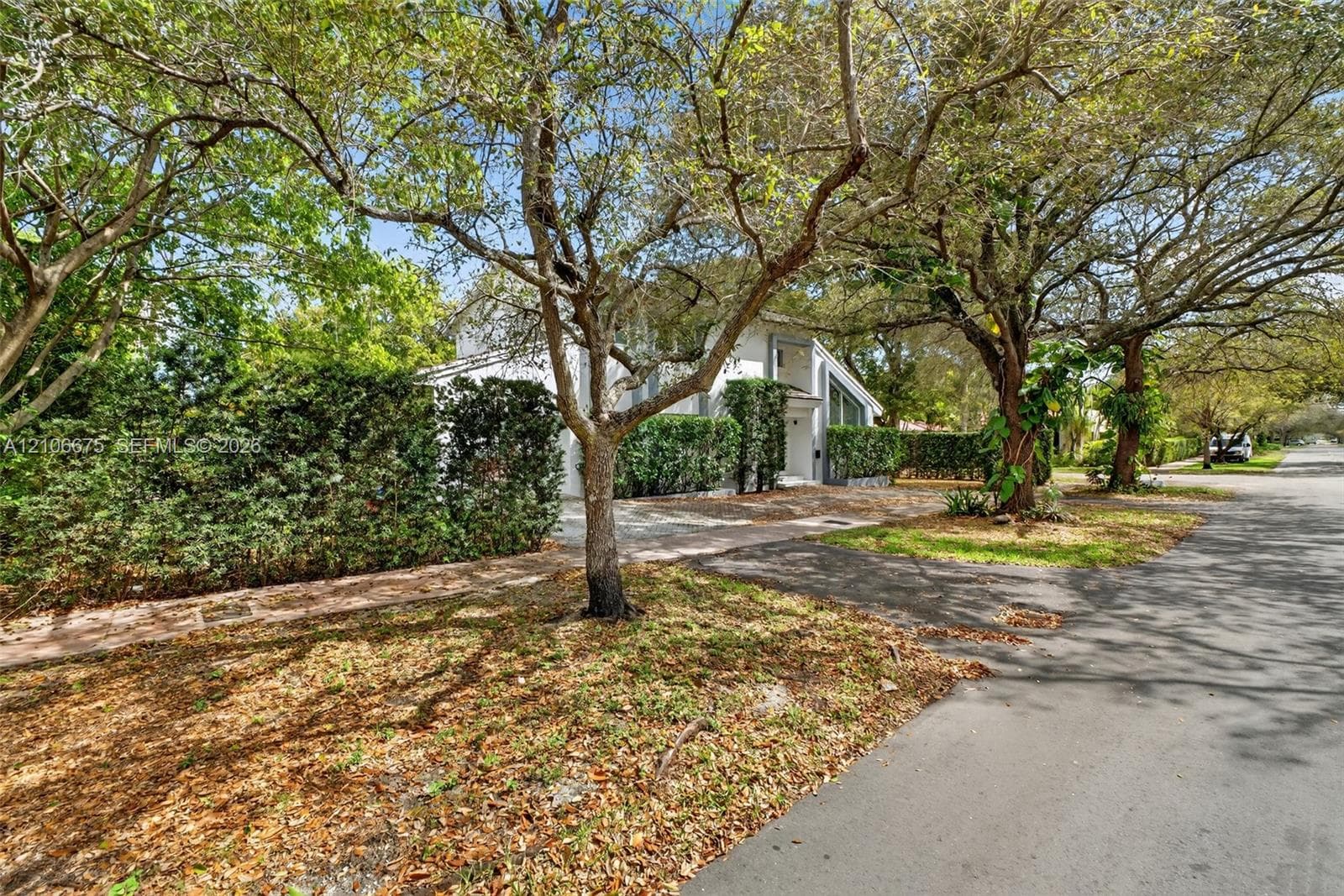 Exterior featuring a two-story residence, asphalt driveway, mature canopy trees, and privacy hedging