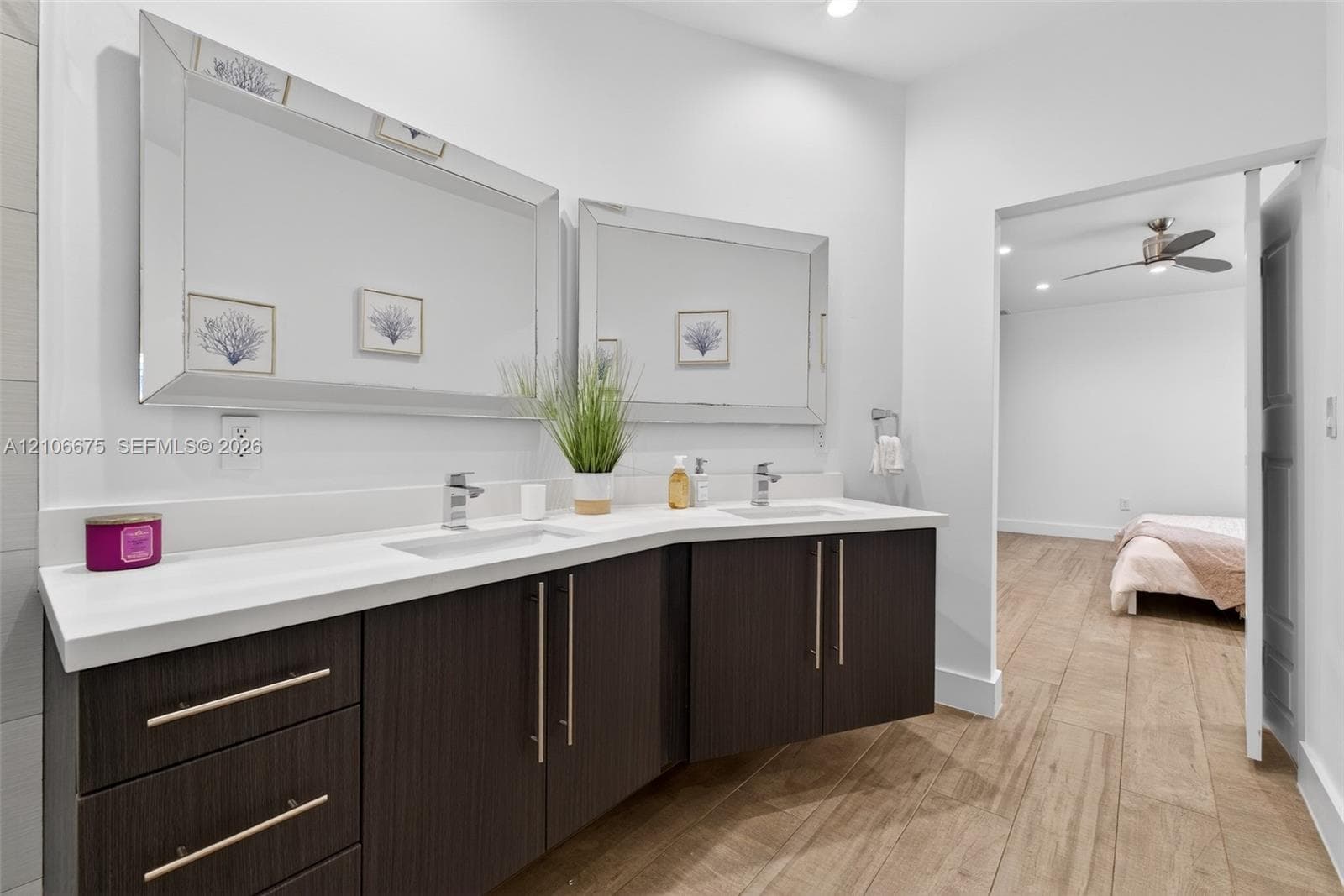 Floating vanity featuring dark wood-finish cabinetry, dual under-mount sinks, light-toned stone-style countertop, and beveled-edge wall mirrors